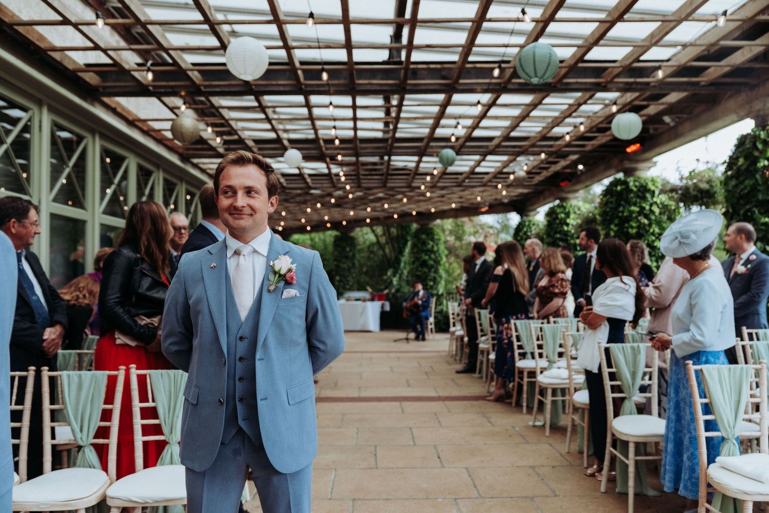 Smiling groom in light blue suit standing in decorated outdoor wedding ceremony venue.