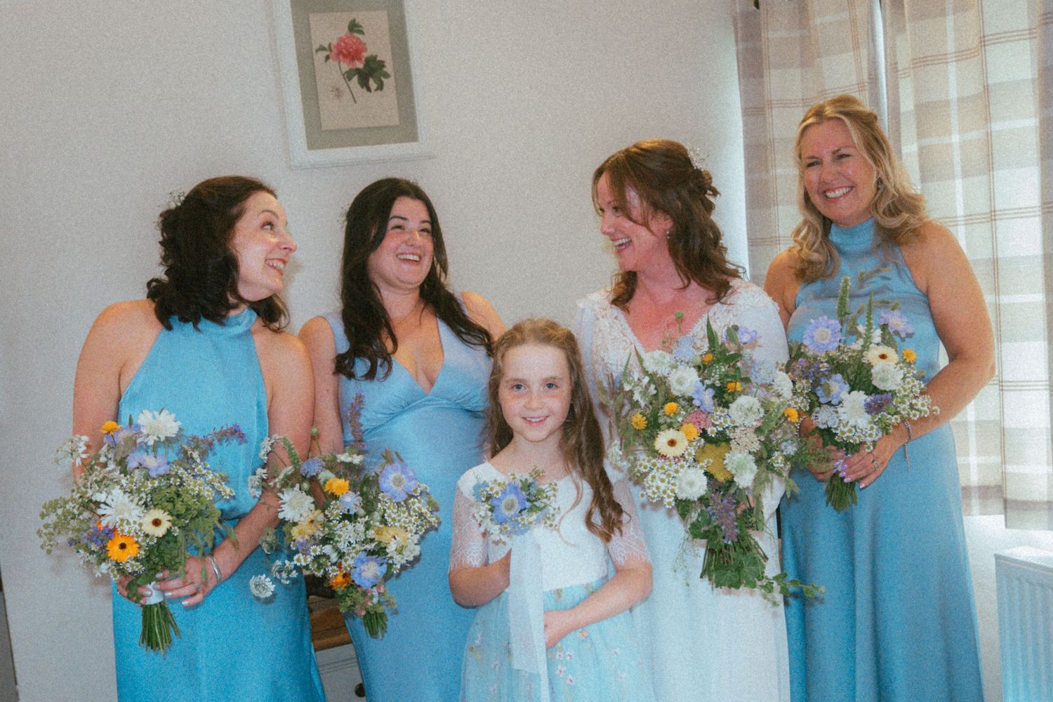 Bride and bridesmaids in blue halter dresses holding wildflower bouquets with a young flower girl in white.