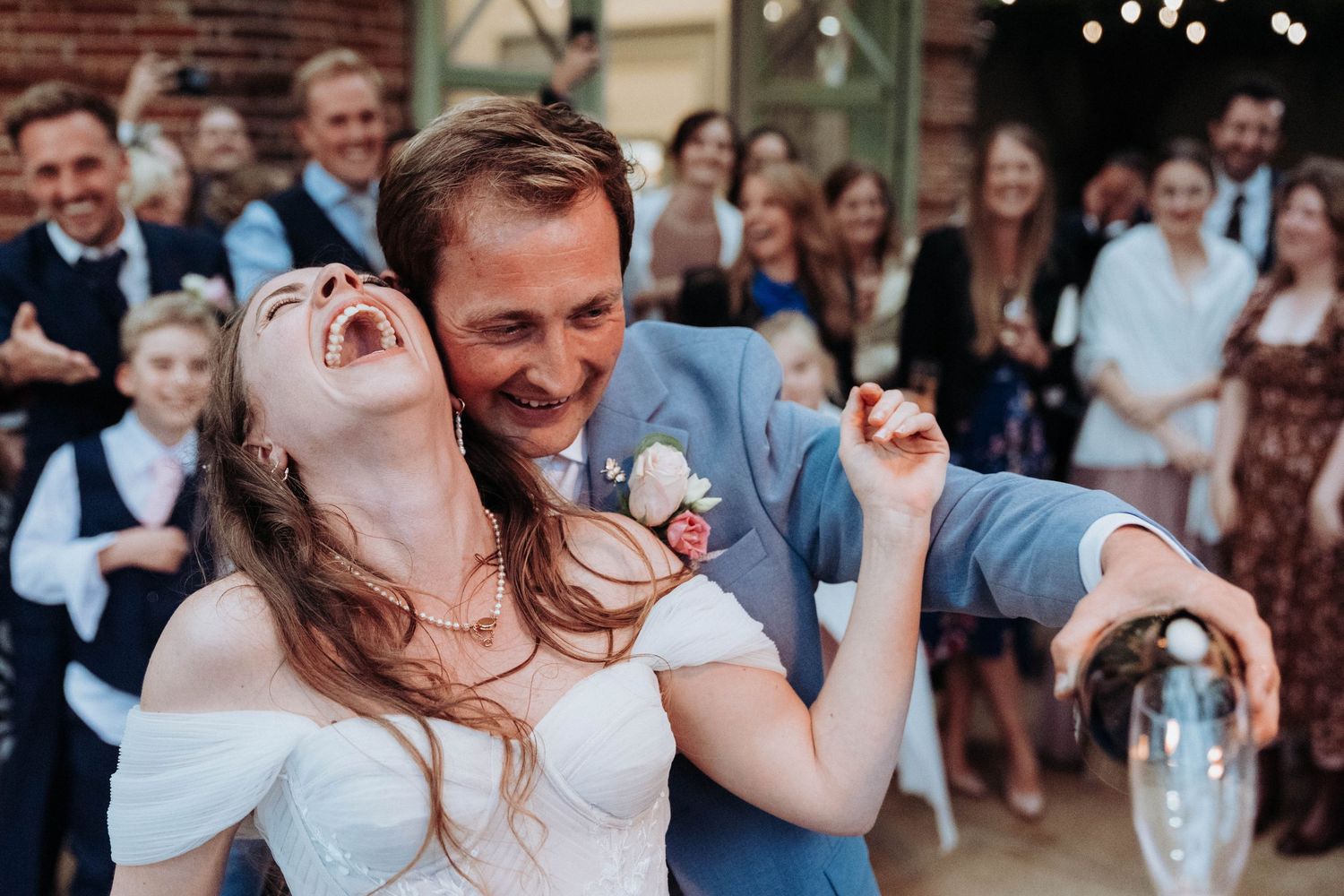 Joyful bride and groom dancing and laughing together at their wedding reception surrounded by cheering guests.
