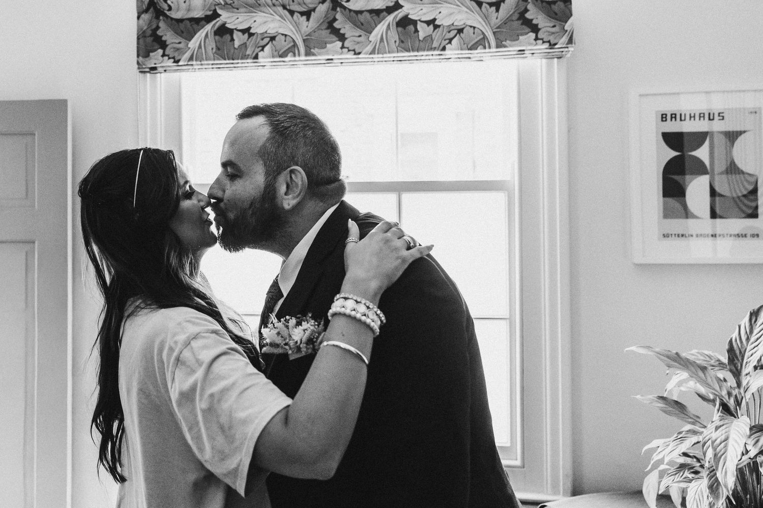 Black and white photo of bride and groom sharing a tender first look kiss indoors.