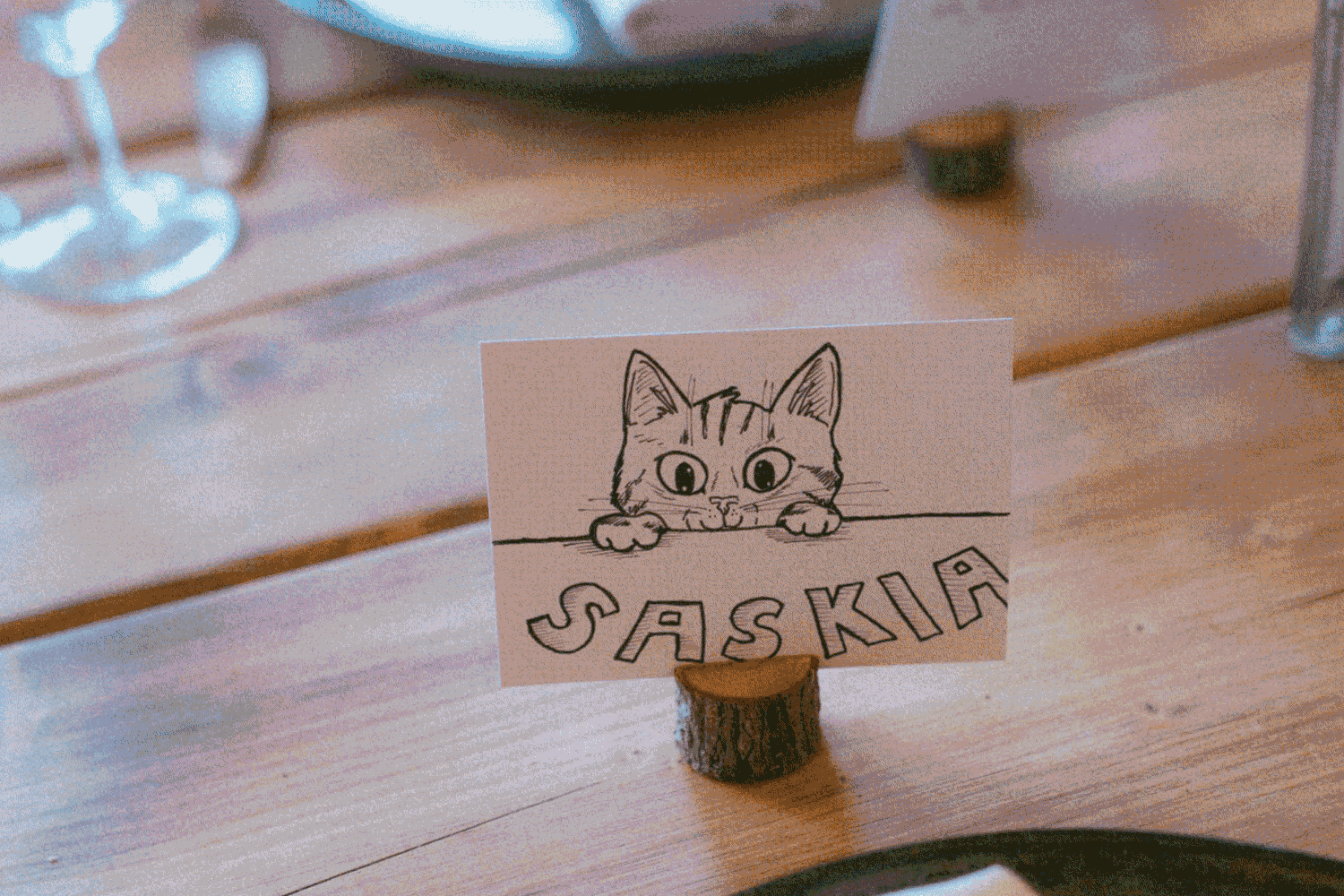 Handmade place card with a cute cat illustration displaying the name Saskia on a wooden table.