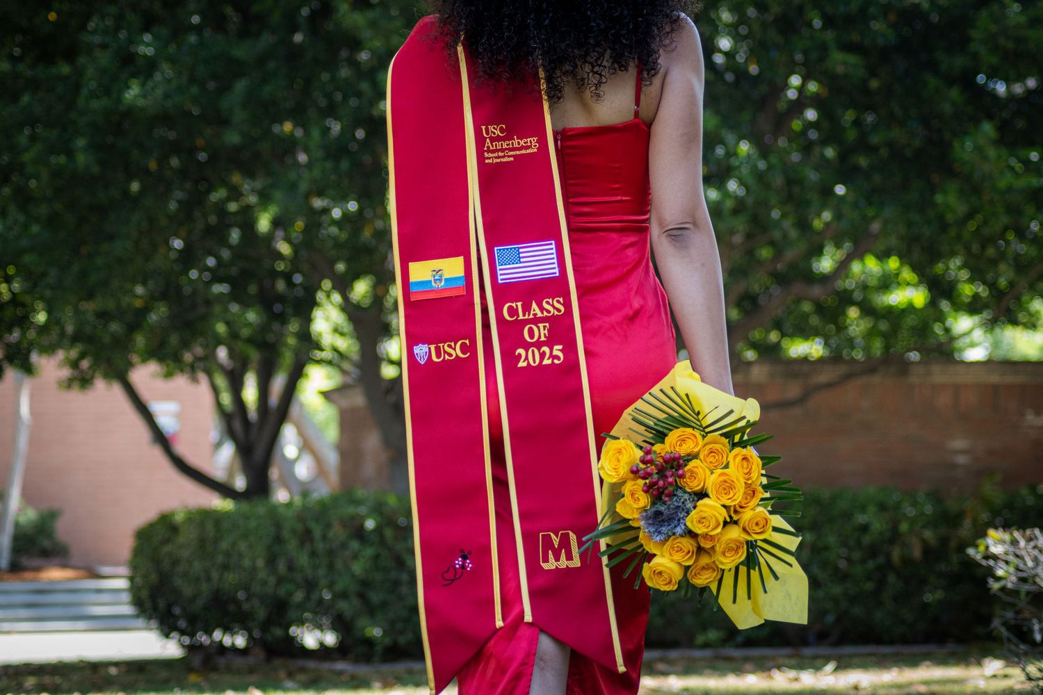 Graduation stole and red dress with sunflowers against garden background.