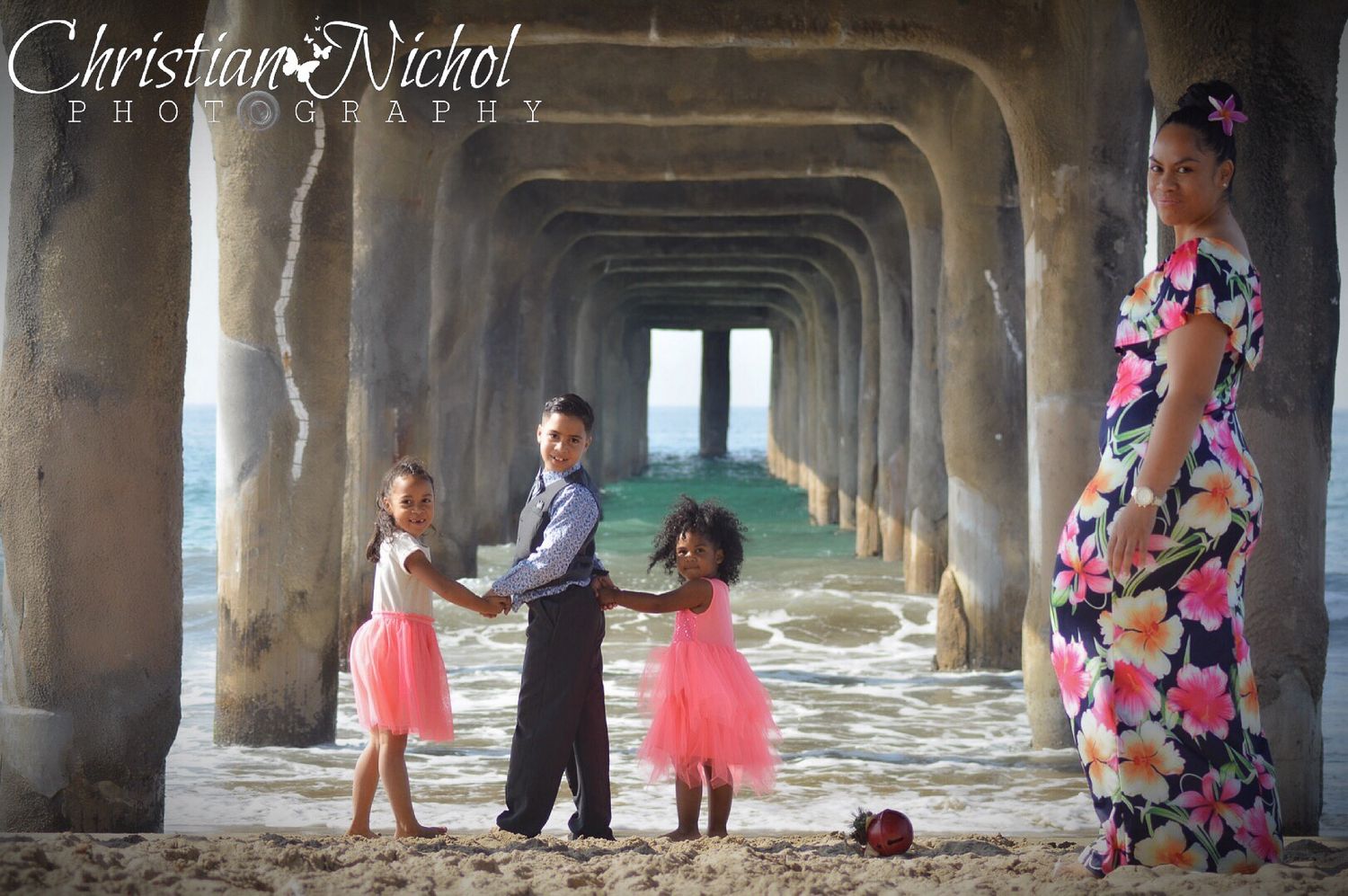 A romantic couple walks through a stone colonnade archway decorated with pink floral arrangements.