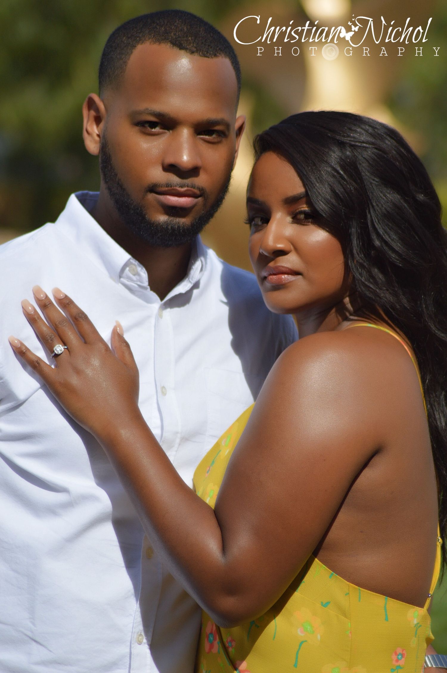 A couple poses intimately for an engagement photo, the woman wearing a yellow dress and diamond ring, by Christian Nichol Photography.