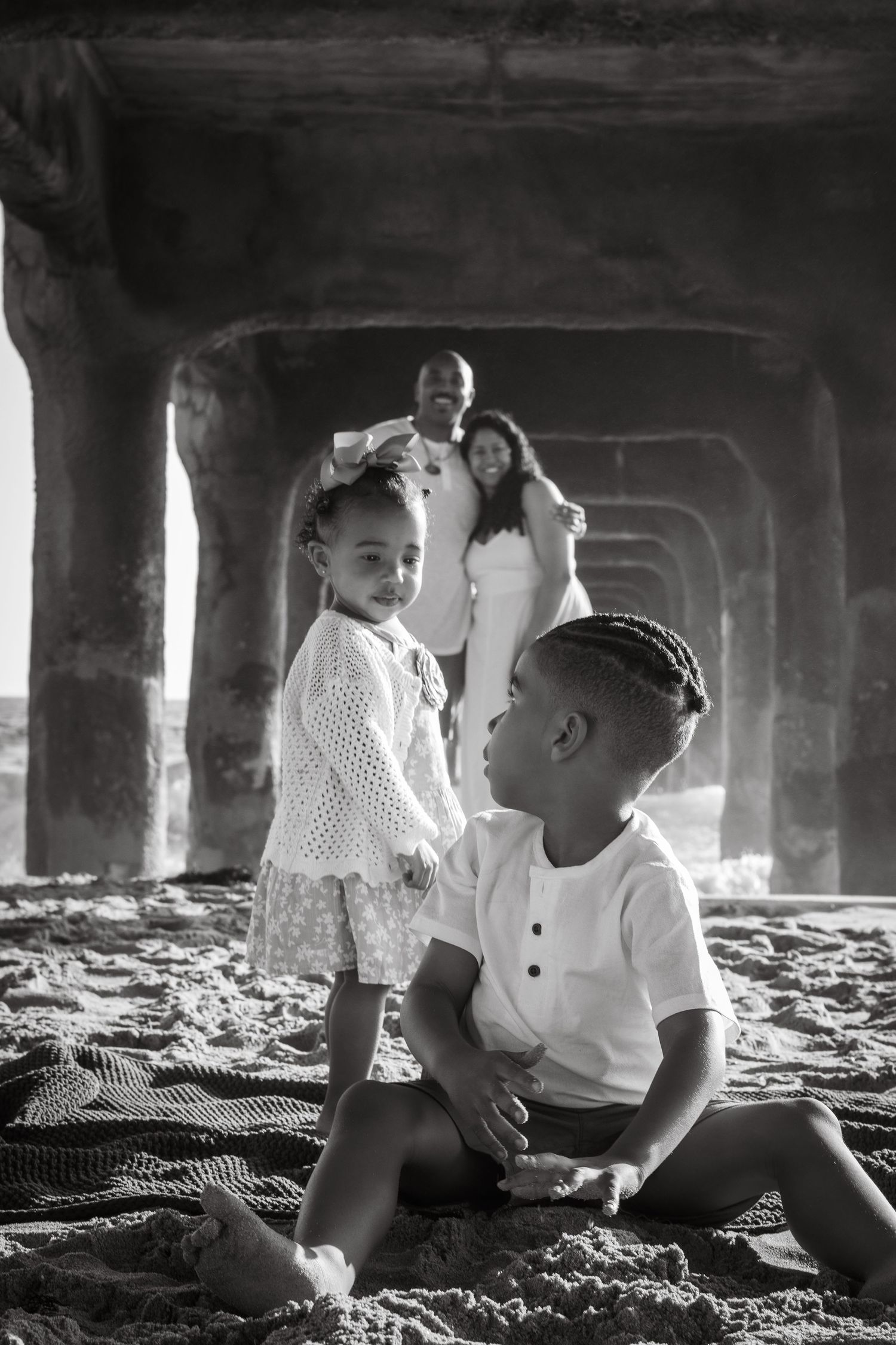 A romantic black and white photo series showing a couple sitting together under a bridge on a sunny day.
