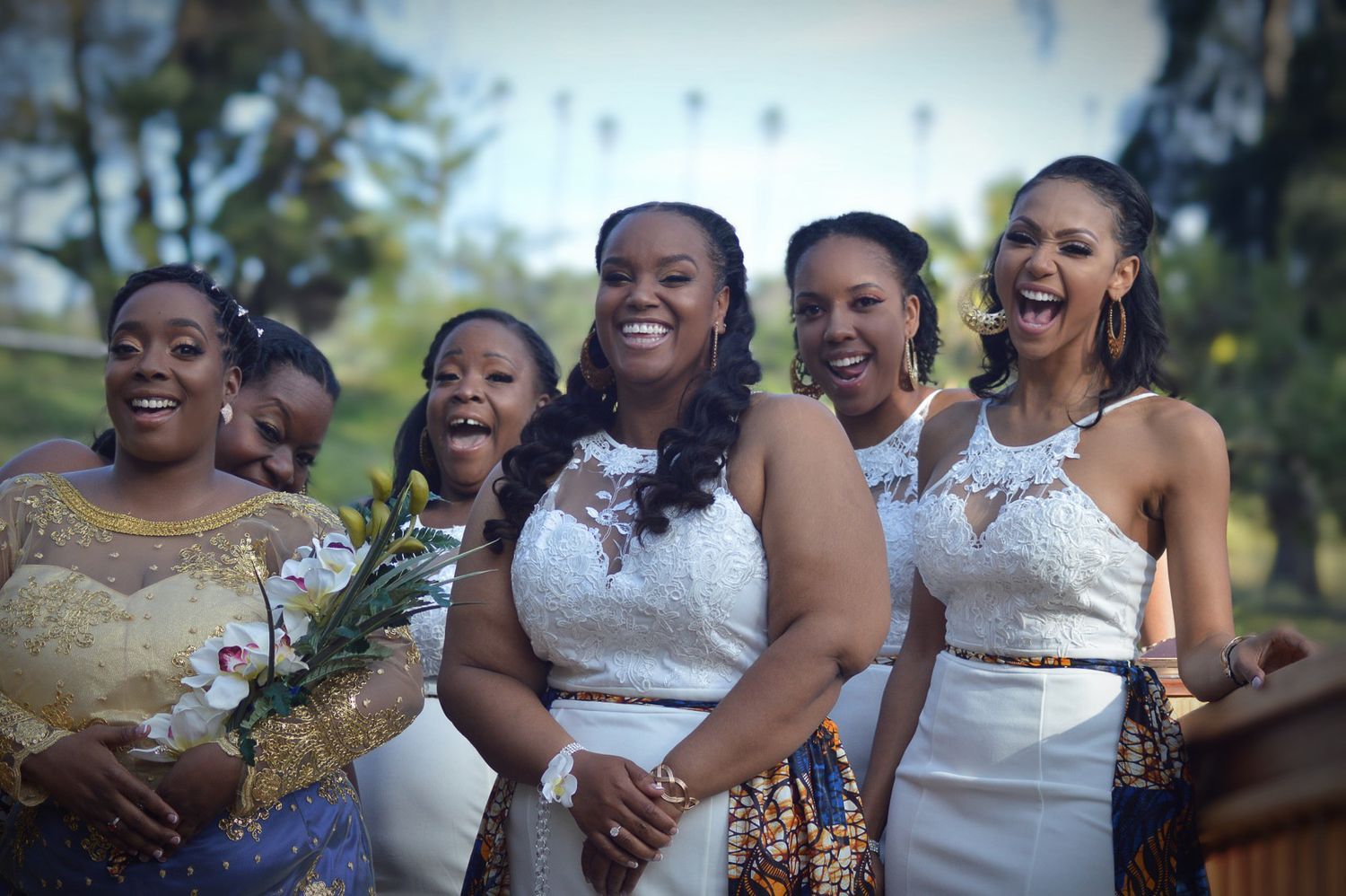 Joyful bridal party in white and colorful dresses laughing outdoors at a wedding celebration.
