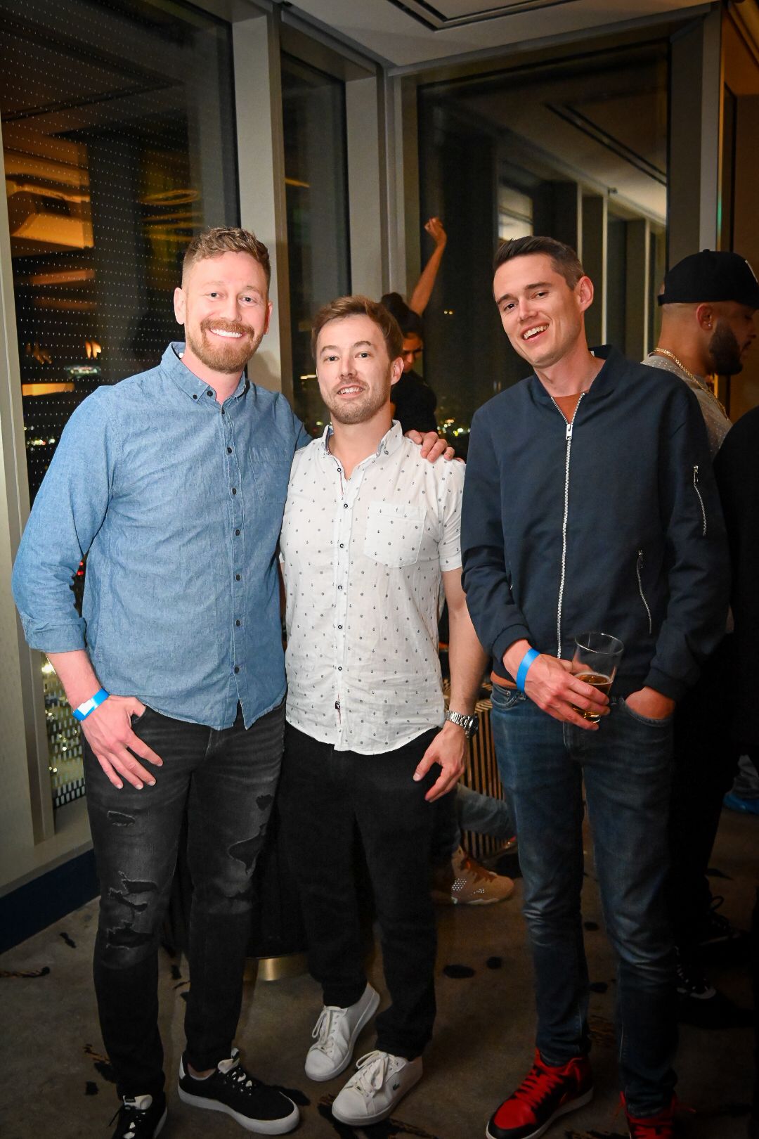 A group of friends in casual attire pose together at an indoor event space.