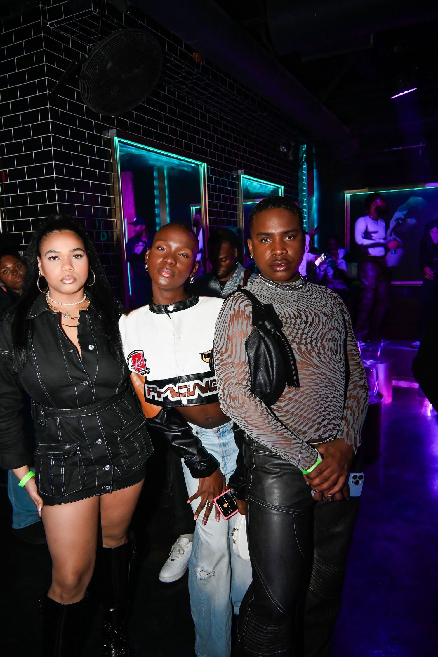People pose together at a nightclub with neon lighting and brick walls in the background.