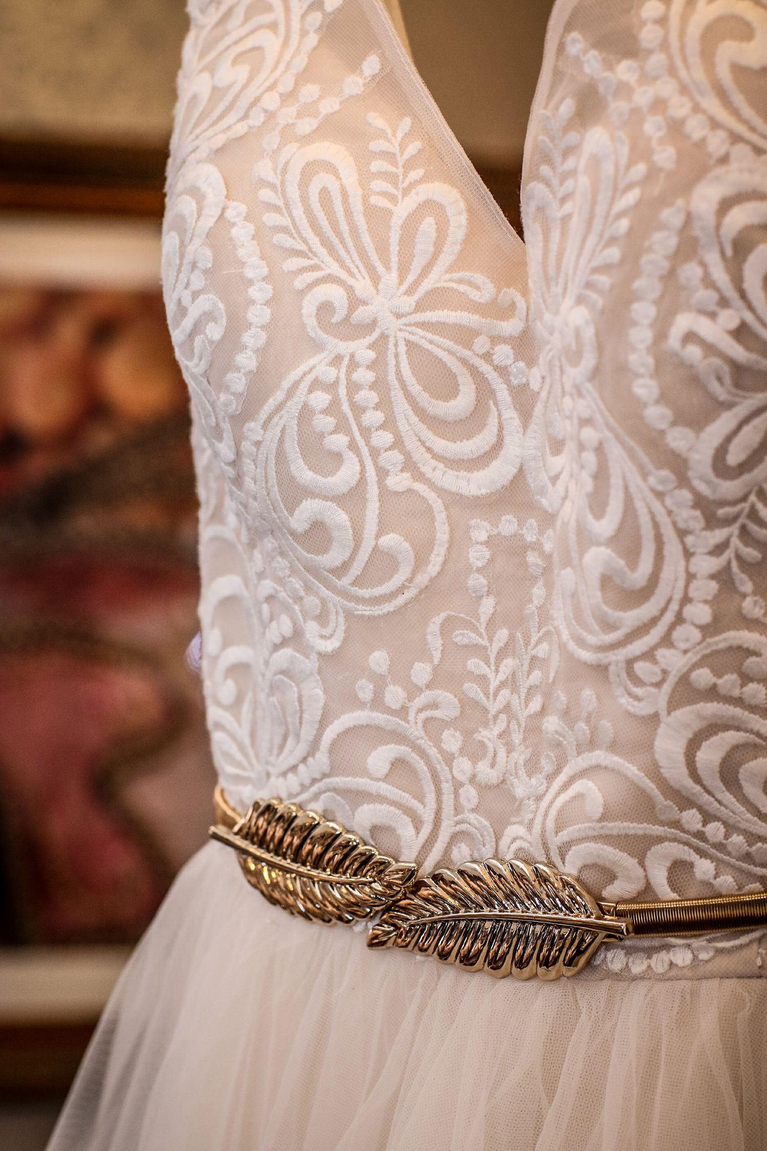 Close-up of a white lace bridal gown with intricate embroidery and a gold feather belt at the waist.