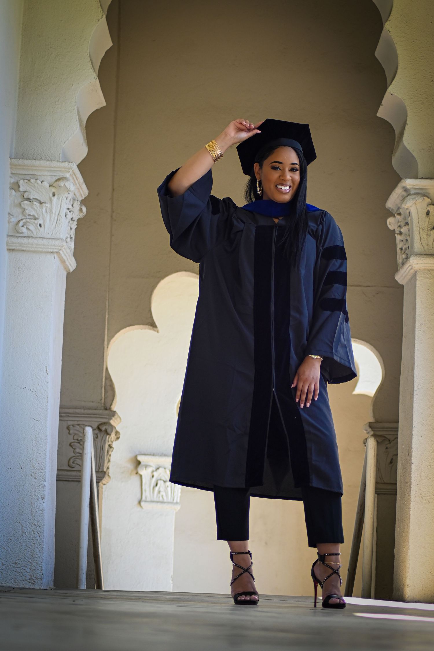 Graduate in doctoral regalia strikes celebratory pose between architectural columns.