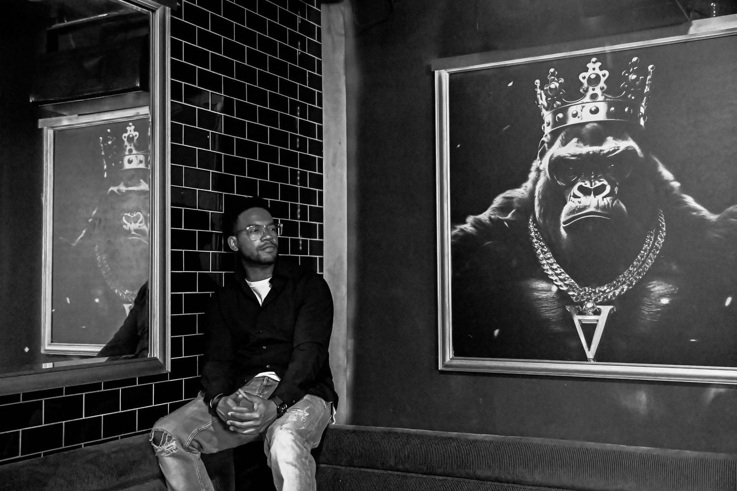 Black and white photo of someone sitting against a brick wall with illuminated artistic projections displayed on windows.