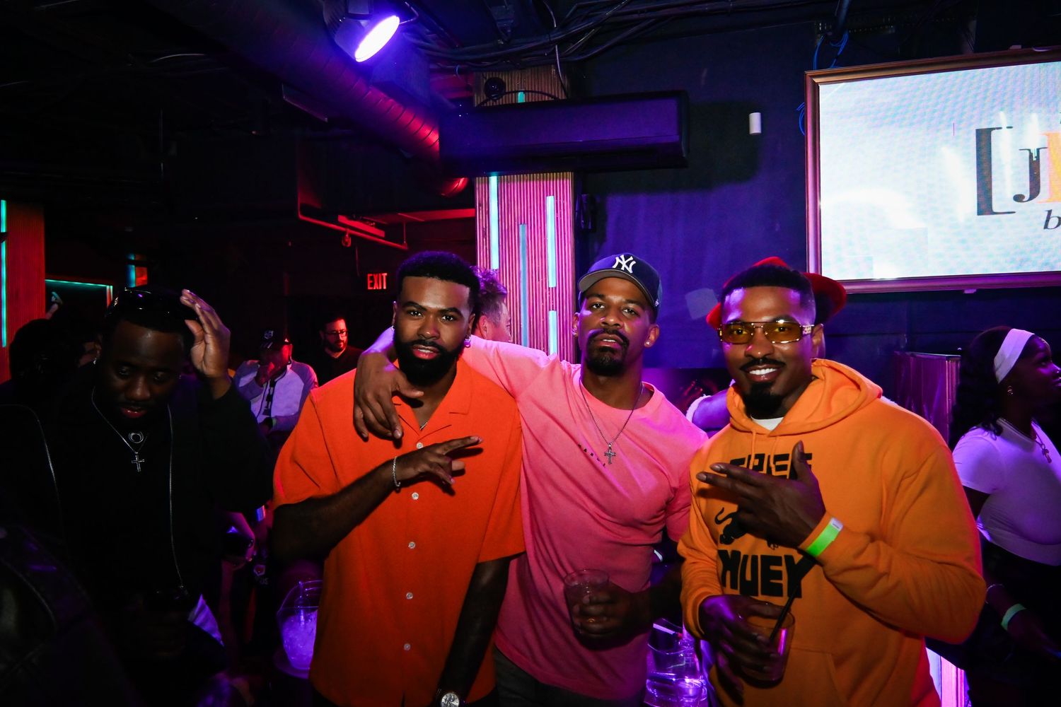 People dancing and celebrating in a nightclub with purple and red lighting effects.