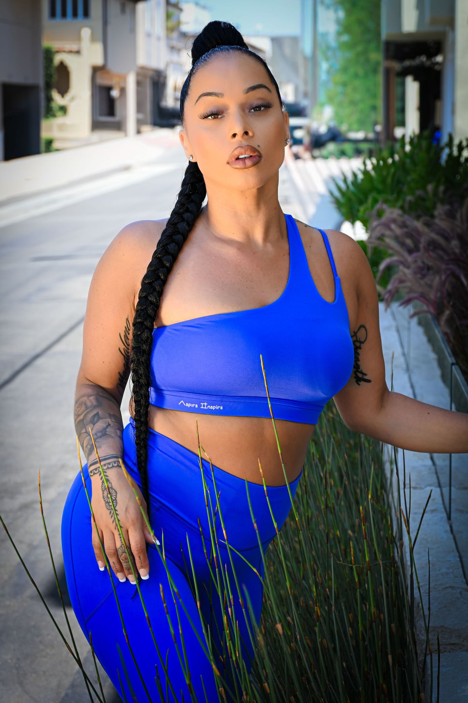 A person in a vibrant royal blue athletic outfit poses outdoors against a backdrop of ornamental grasses.