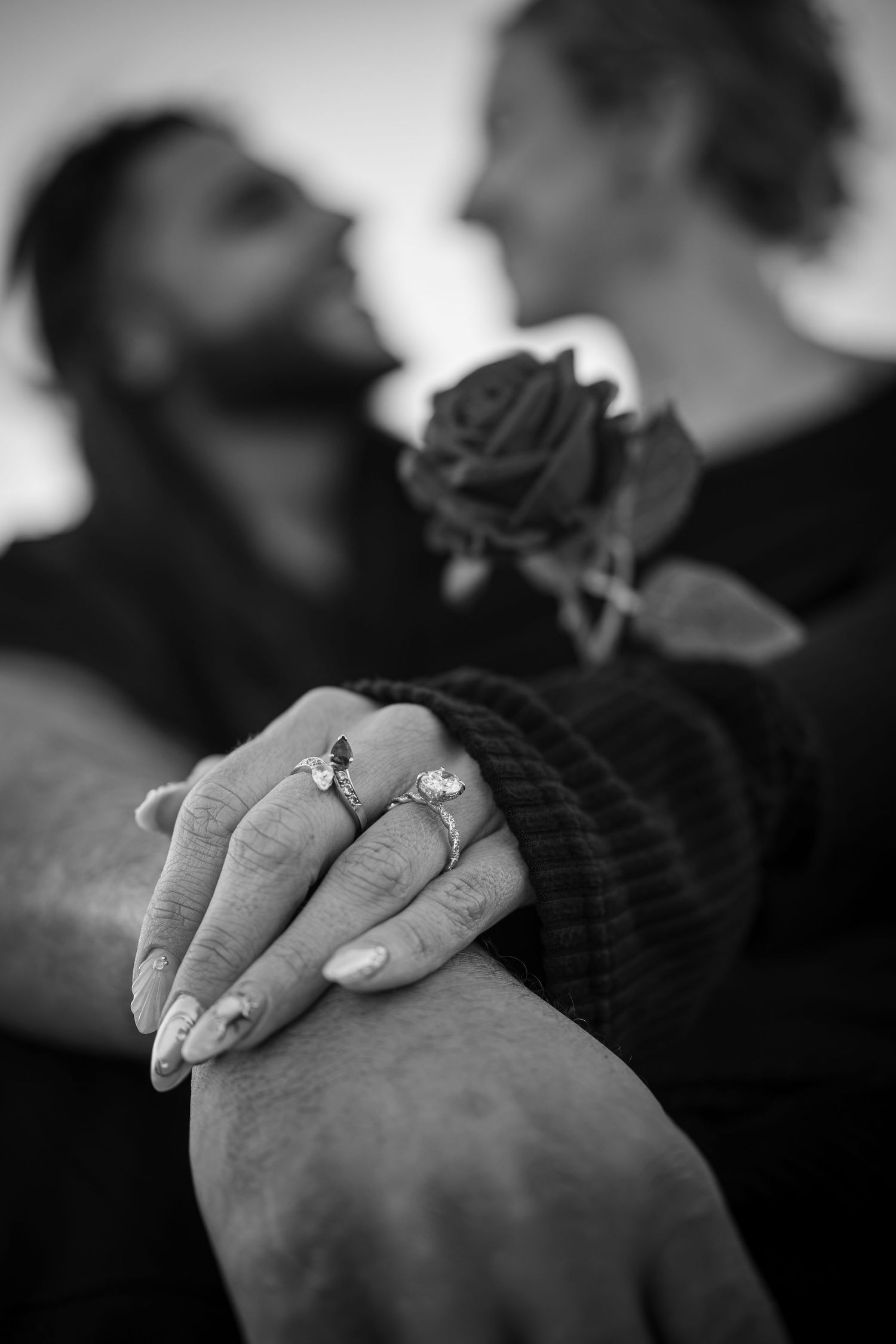 Black and white photo of couple holding hands showing engagement rings with a rose.
