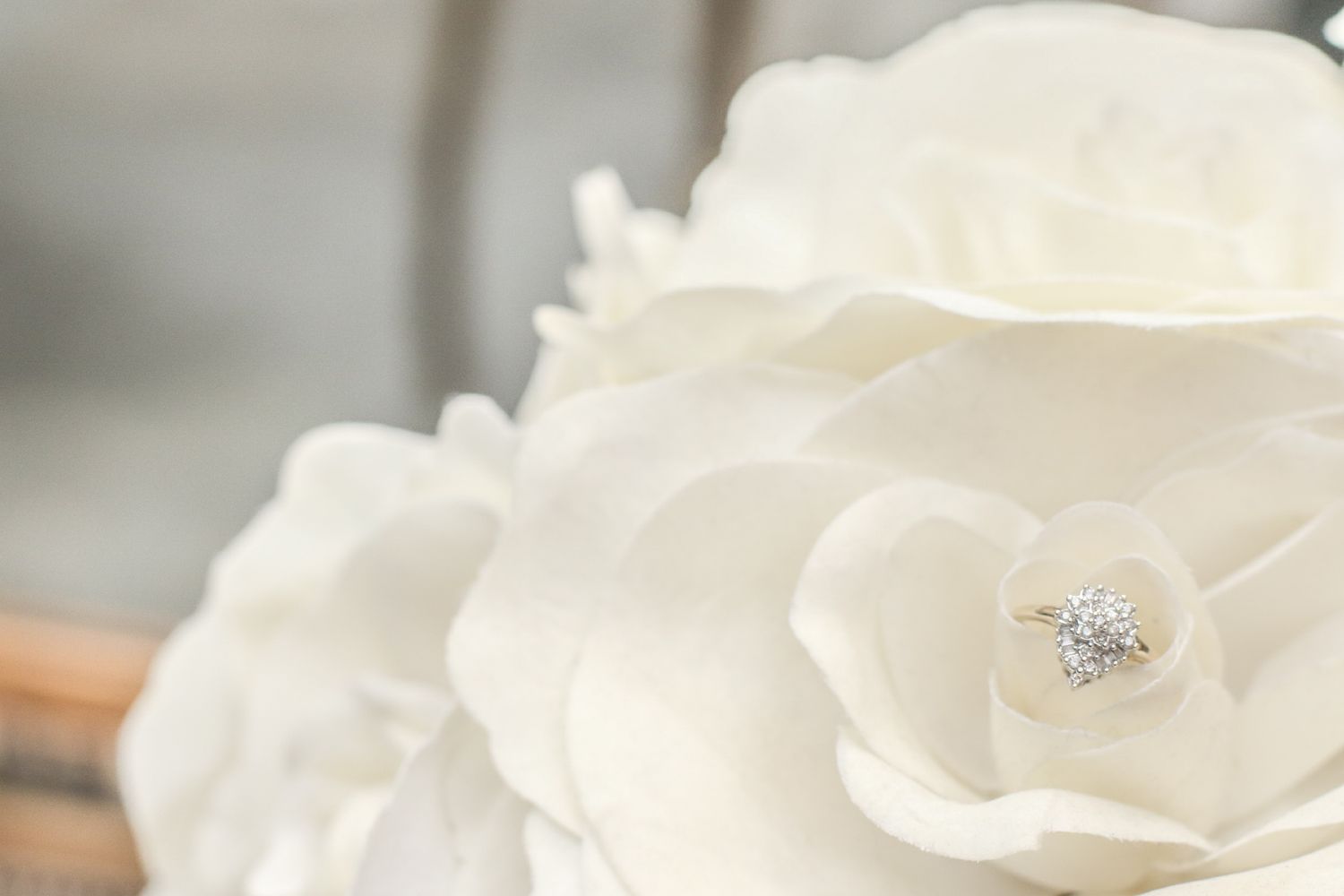 Diamond engagement ring resting on white fabric roses, elegant wedding detail photography.