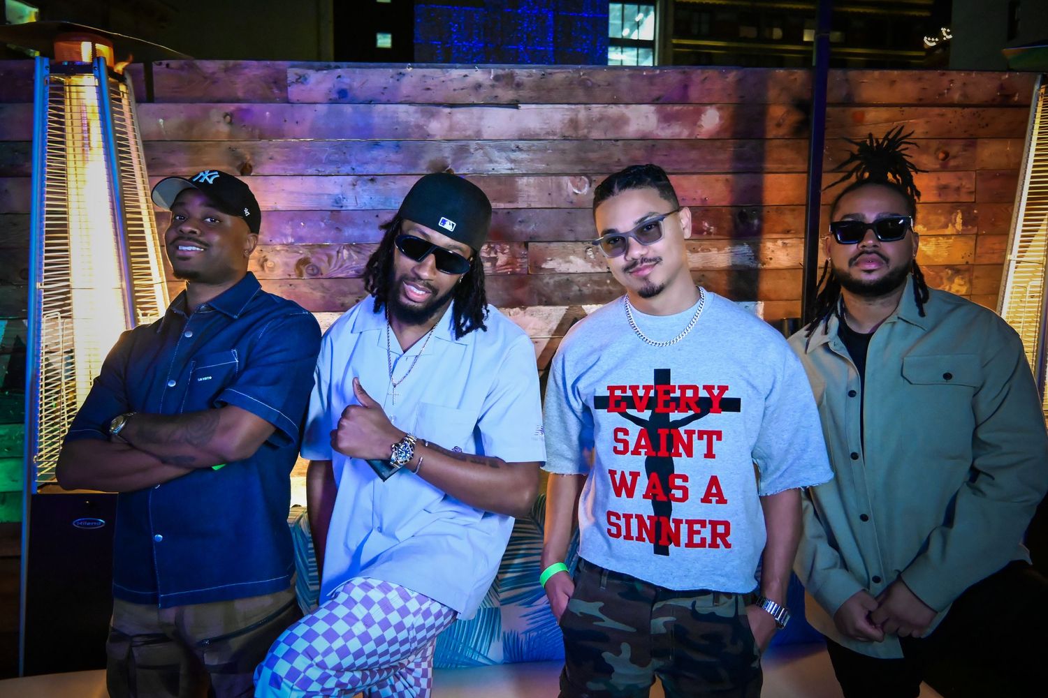 A group of people posing together at a nightclub or bar with colorful lighting and brick walls in the background.