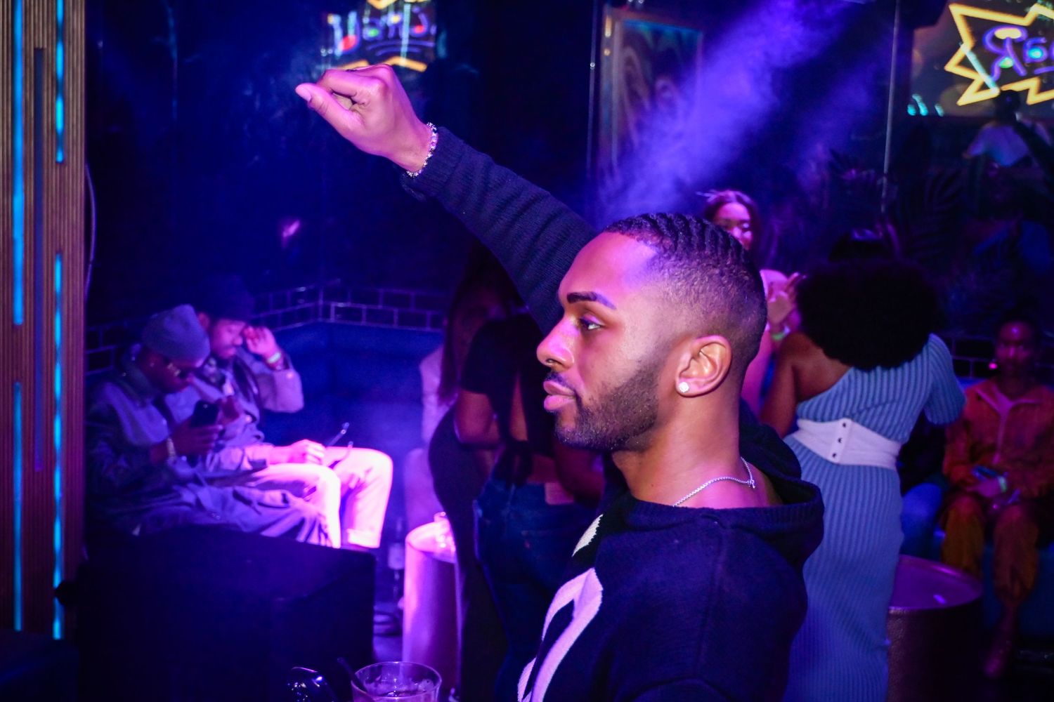 Crowd enjoying a nightclub party with purple lighting and hands raised in the air.