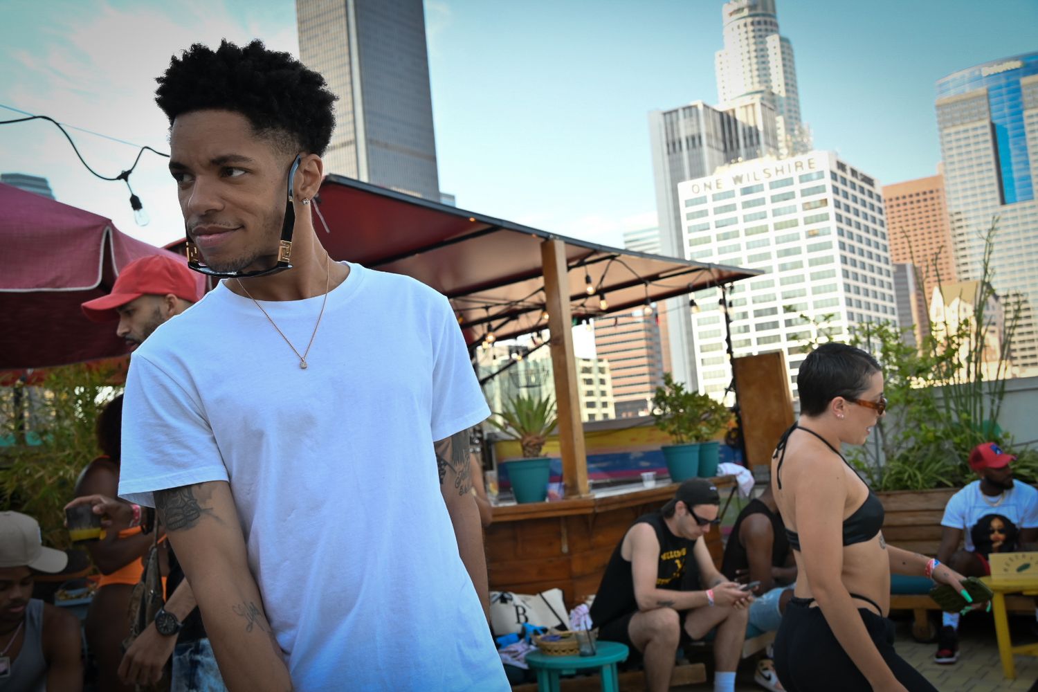 Person in white t-shirt standing at outdoor rooftop venue with city skyline and buildings in background.