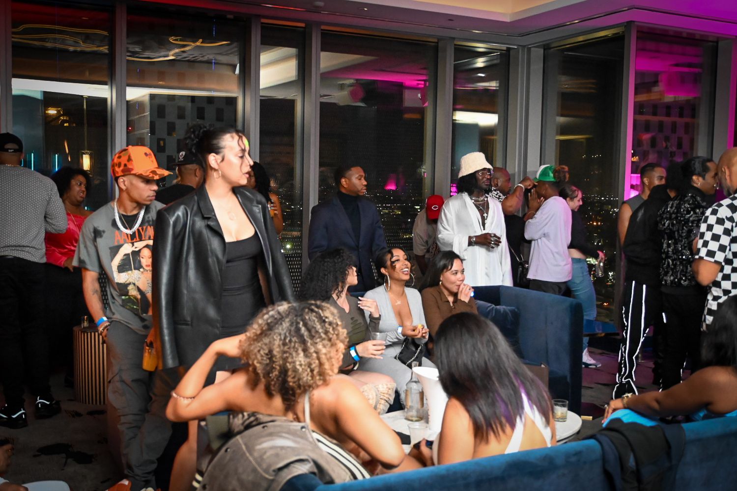 A crowded nightclub scene with people dancing and socializing under purple mood lighting.