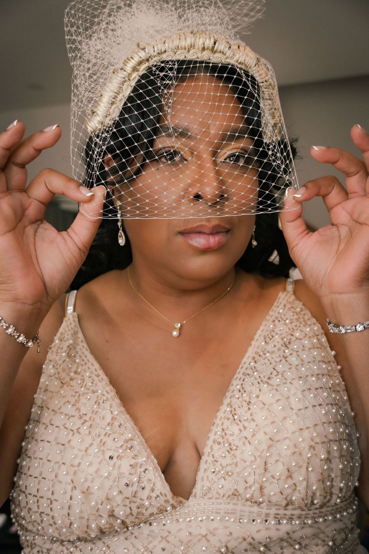 A bride wearing a beaded gown and birdcage veil with pearl accessories poses elegantly for her wedding portrait.