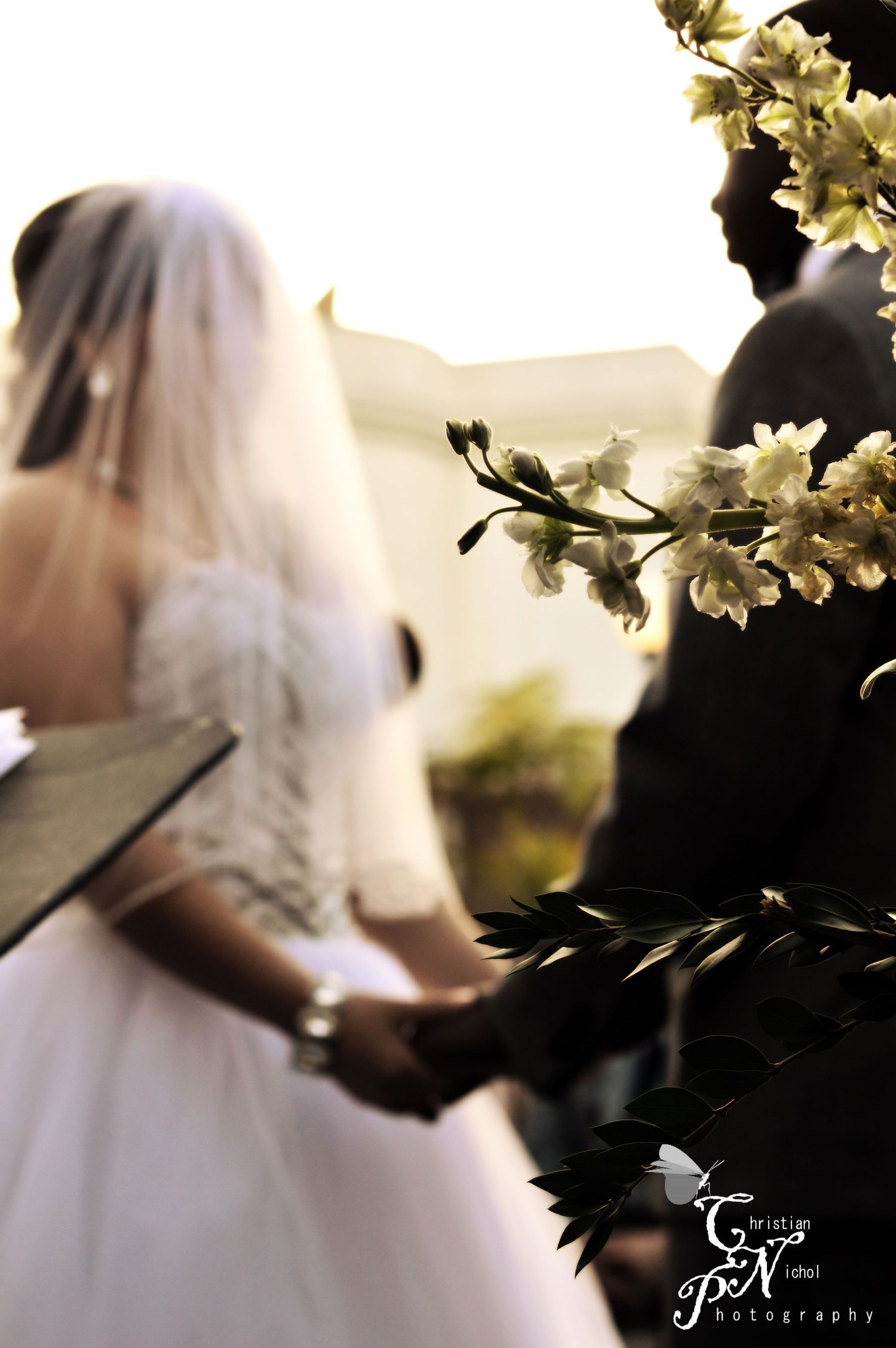 Bride and groom holding hands during outdoor wedding ceremony, white floral blooms in foreground.