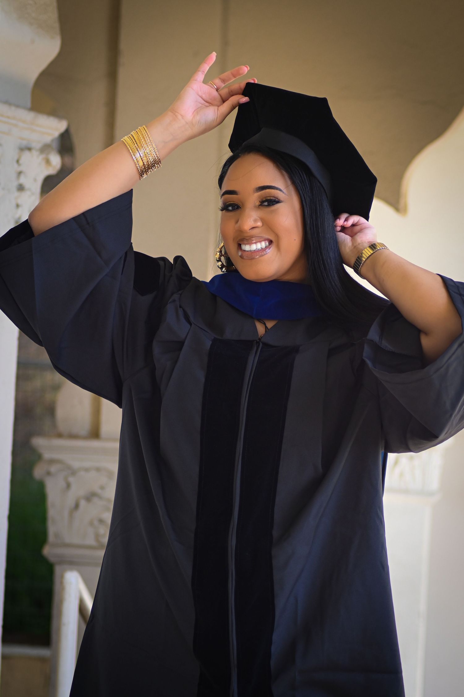 Excited graduate in academic regalia poses with raised arms celebrating achievement.