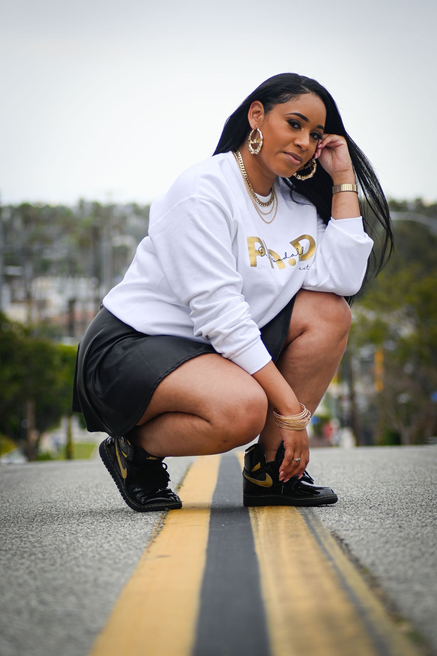 Street style portrait featuring gold jewelry and a white sweatshirt against an urban setting.