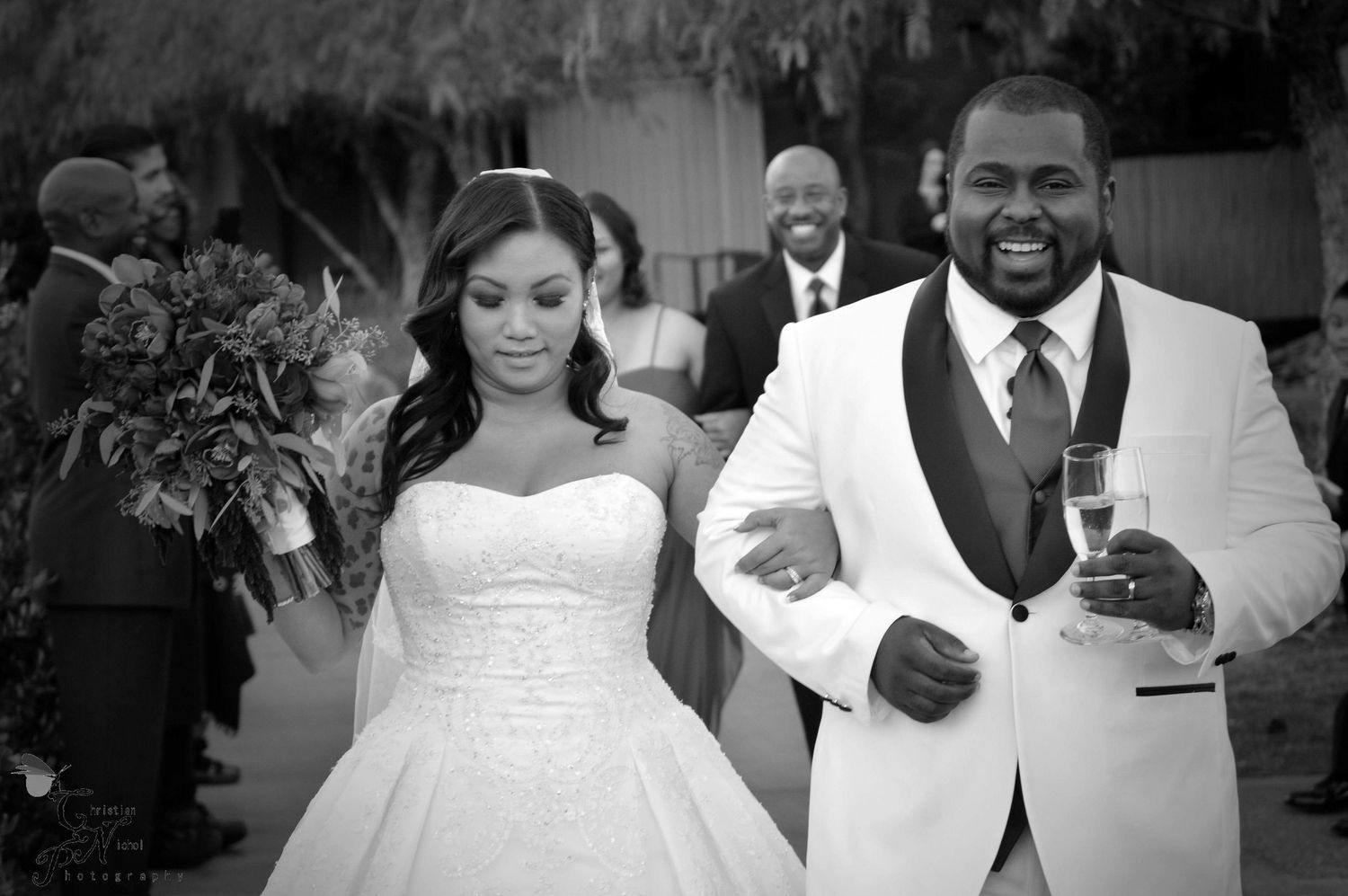 Black and white photo of a bride and groom smiling as they walk together at their wedding reception.