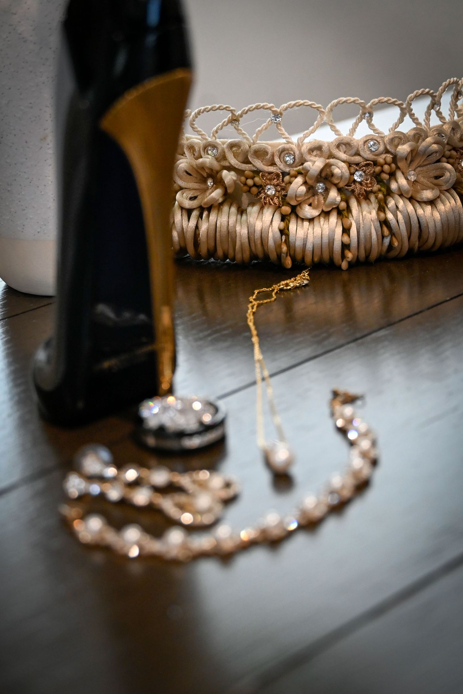 Elegant bridal accessories including gold heels, pearl necklace, diamond pendant, and beaded clutch purse on wooden surface.