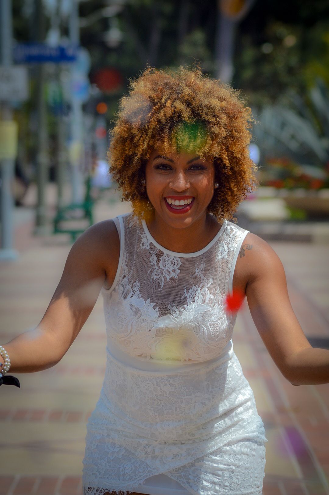 Person in white lace dress smiling and dancing outdoors.