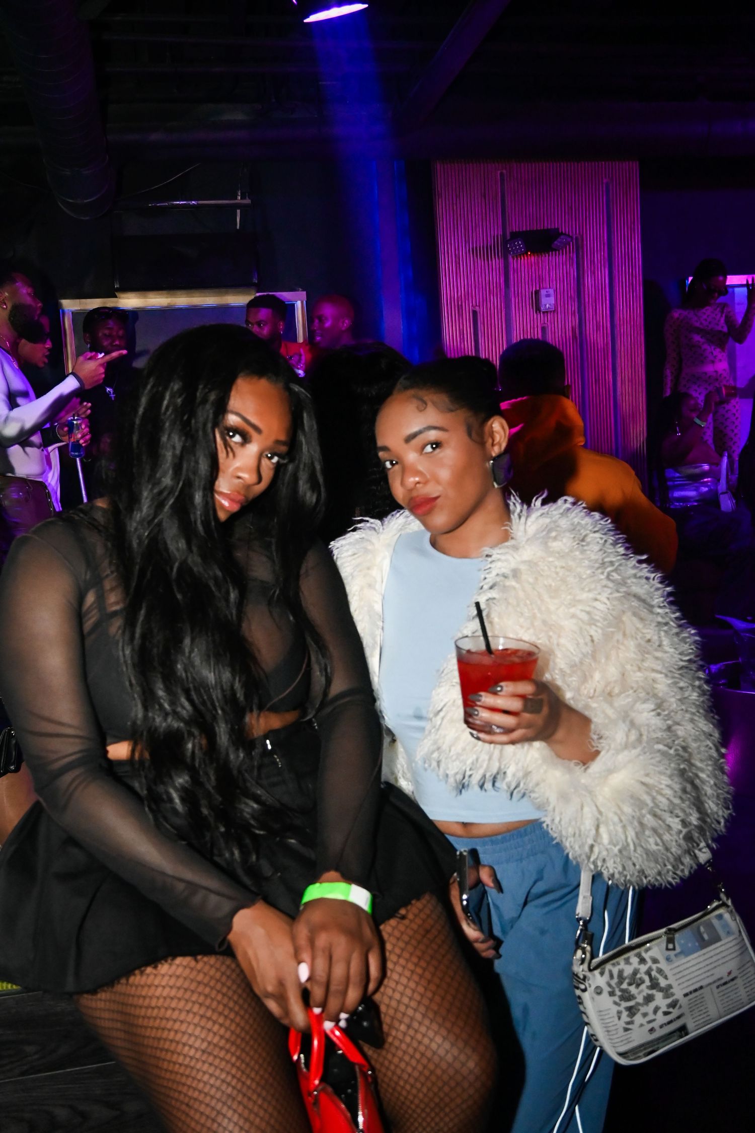 Partygoers in festive attire dance and socialize at a nightclub with blue and purple lighting.