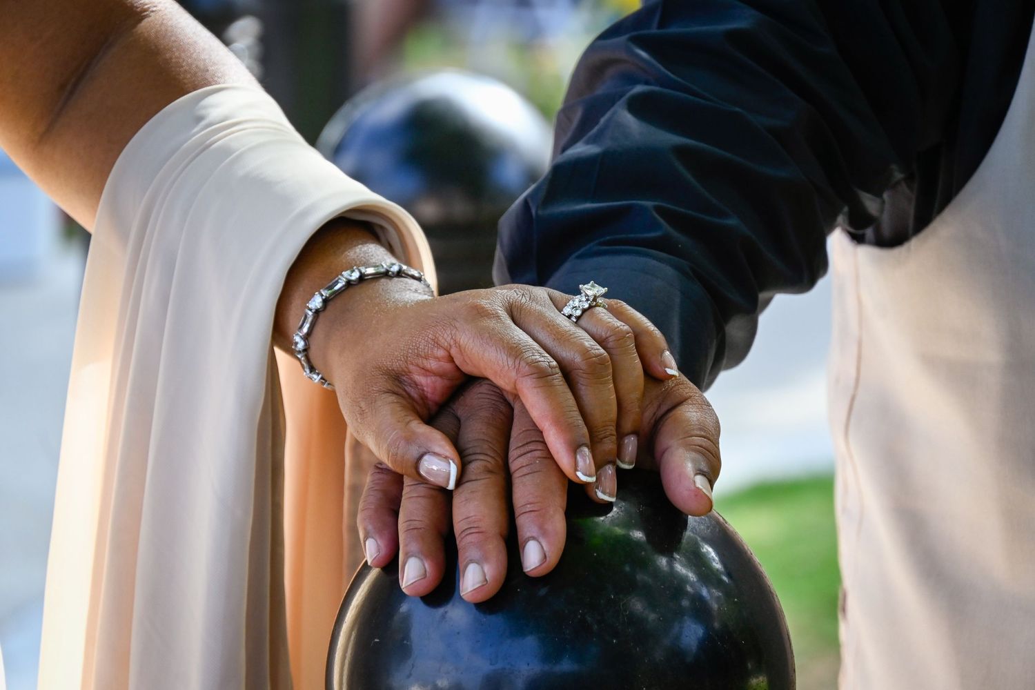 Couple's hands together on a dark bowling ball, woman wearing diamond ring and bracelet, wedding or engagement photo.