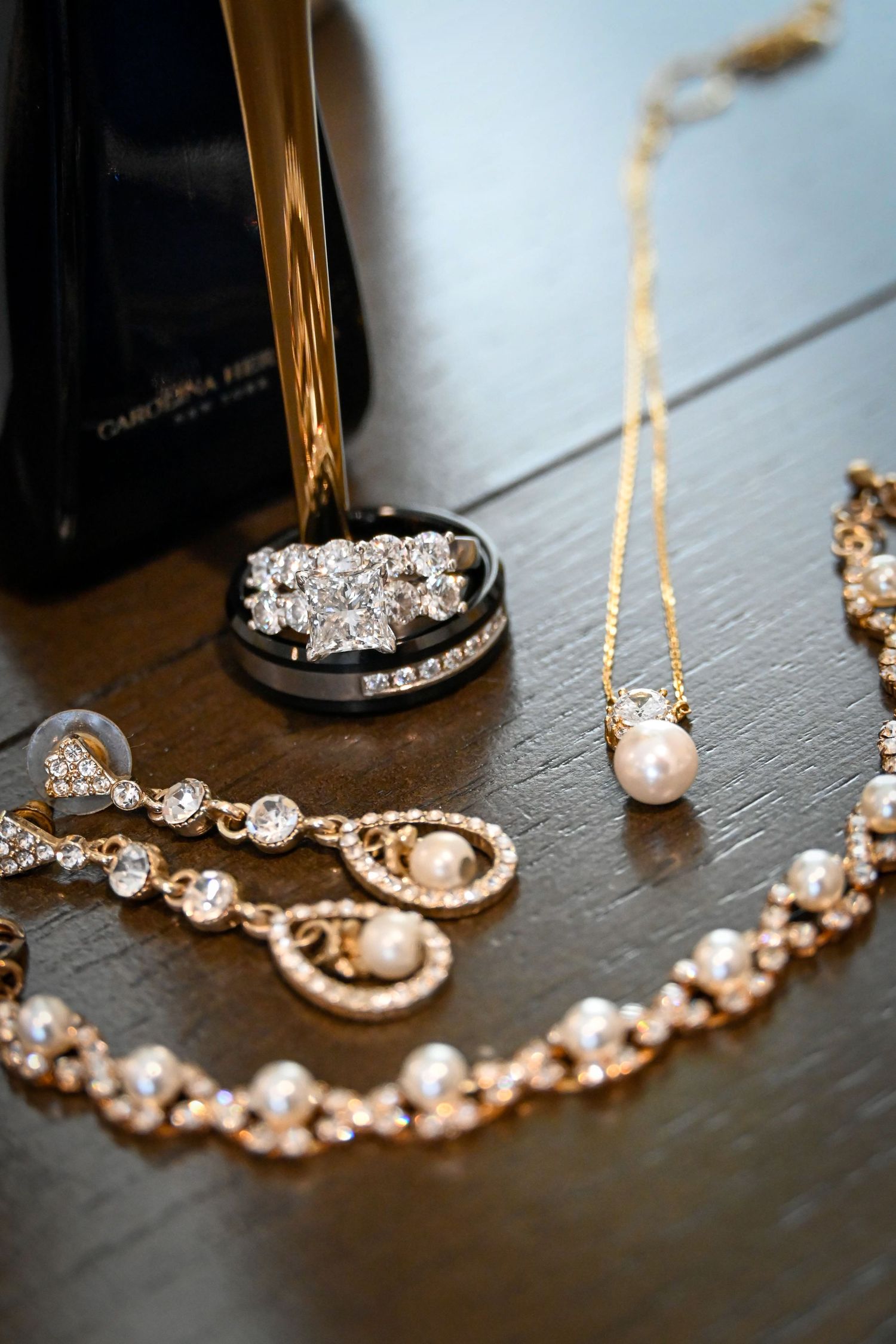 Elegant bridal jewelry set featuring diamond rings, pearl necklace, gold bracelet, and crystal earrings beside Carolina Herrera perfume.
