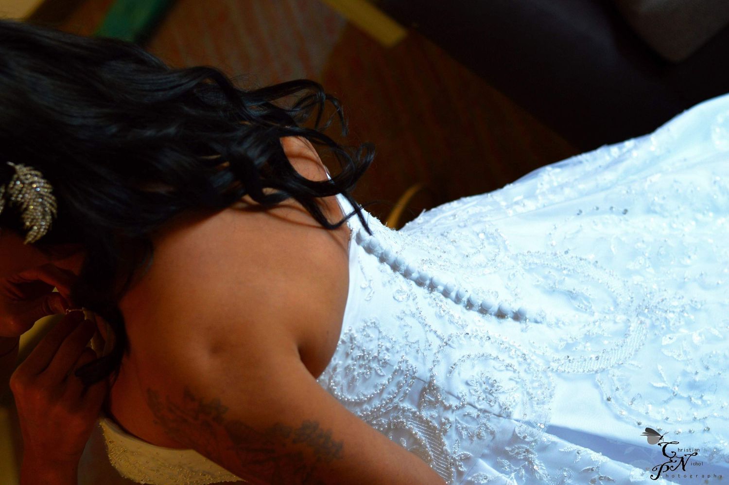 Bride in white lace wedding dress with pearl necklace, dark hair adorned with decorative accessory, viewed from above.