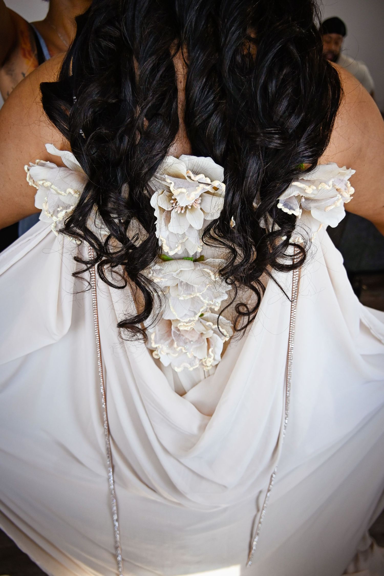 Back view of bride in white gown with floral details and cascading dark curls at wedding.