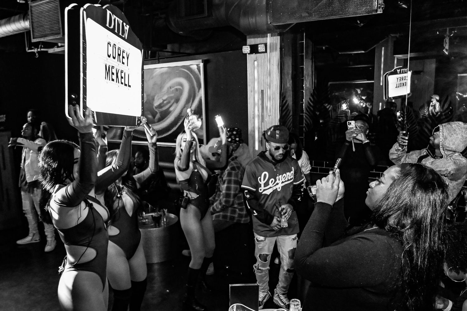 People in a dark nightclub or bar setting with silhouettes visible against dim lighting and neon signs.