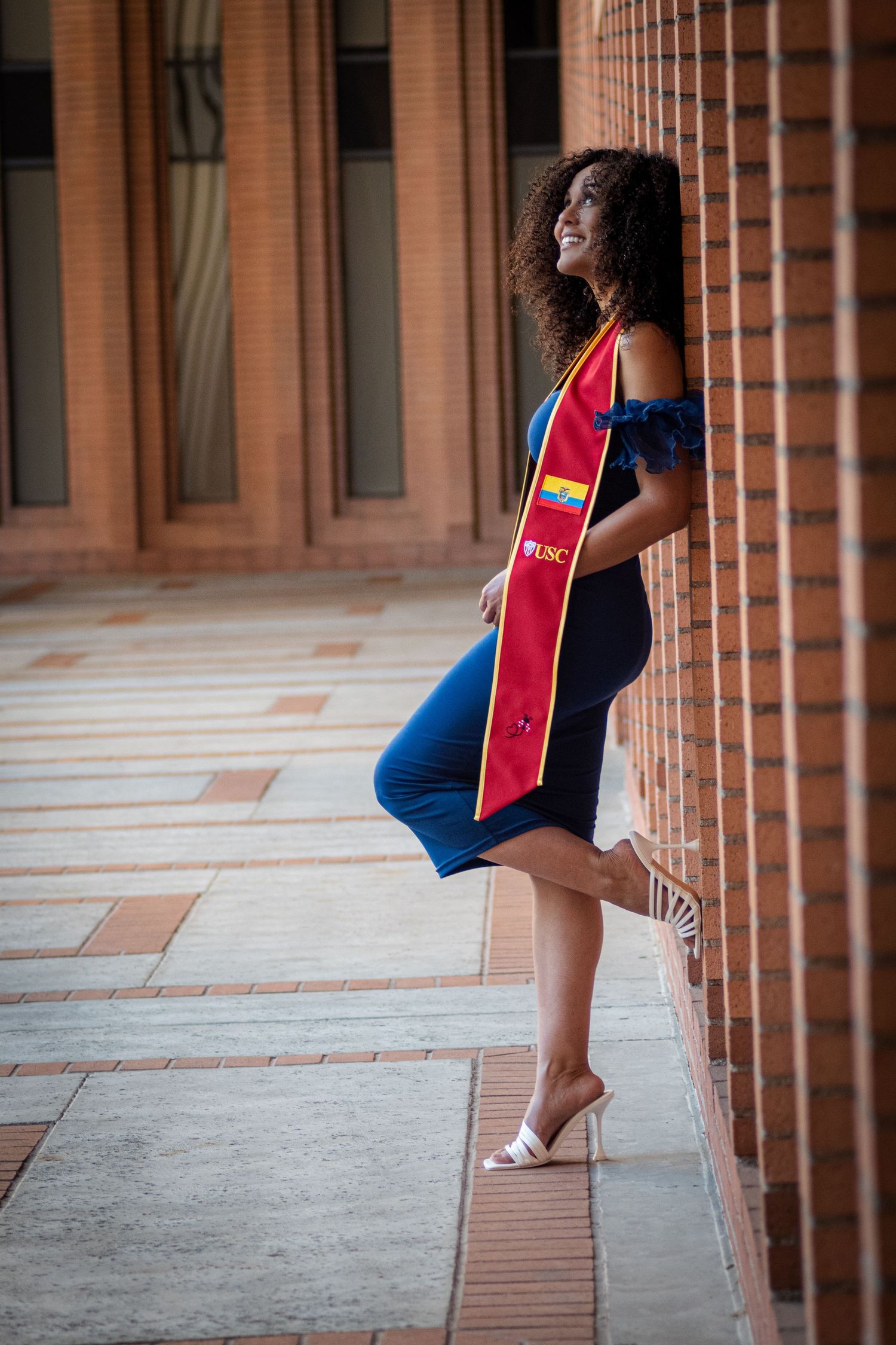 Graduate in blue dress poses elegantly between brick columns.
