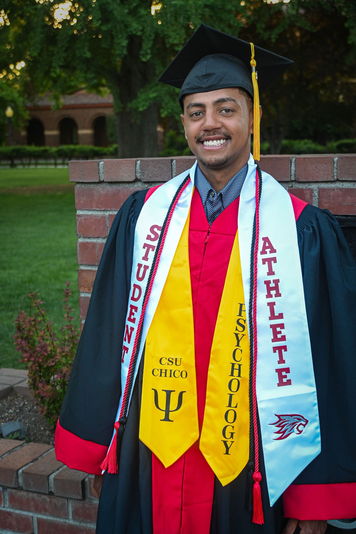 Graduate in cap and gown wearing psychology and athlete graduation stoles at CSU Chico outdoor ceremony.