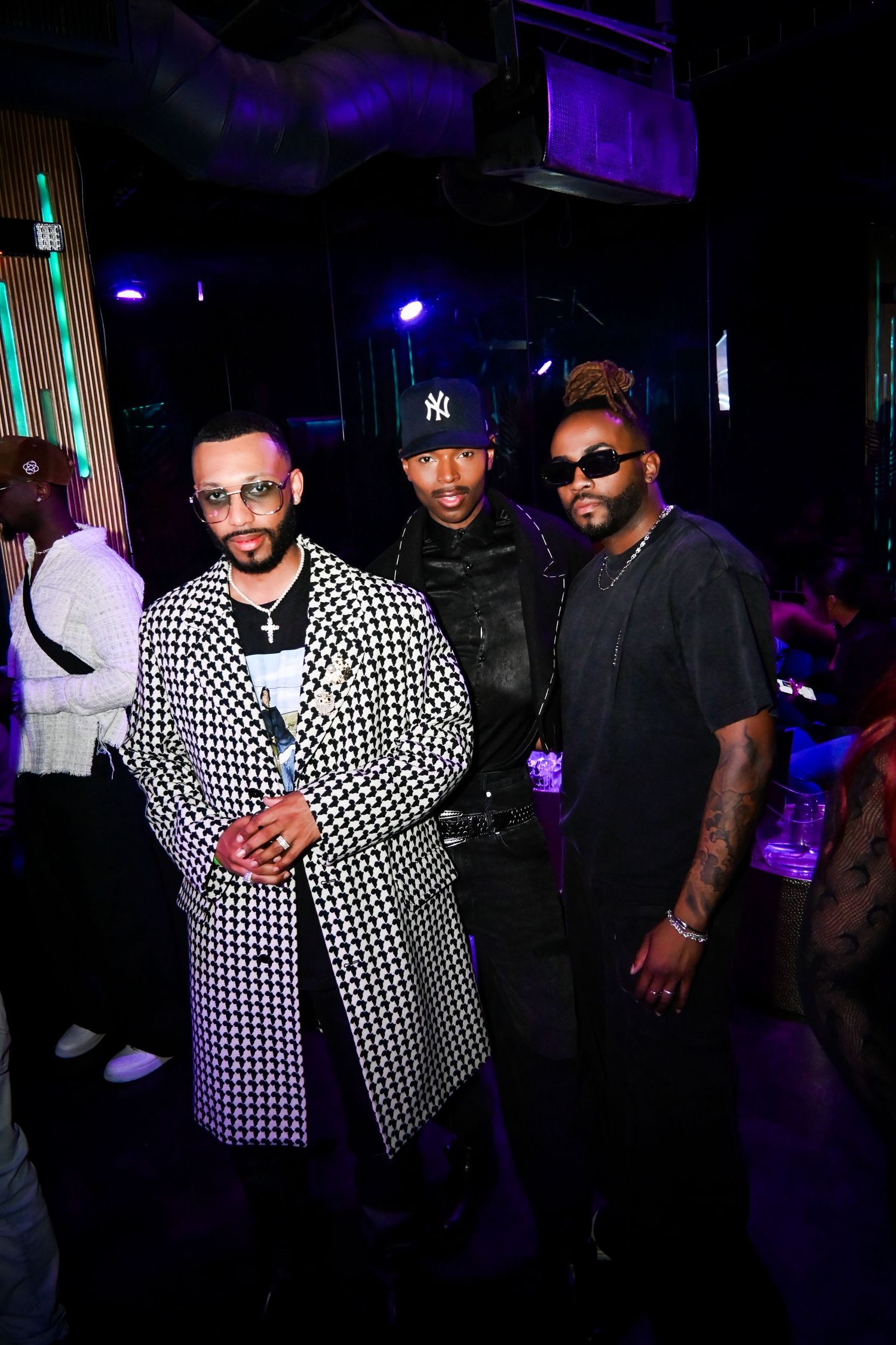 Three people pose together at a nightclub with purple lighting and dark ambiance in the background.