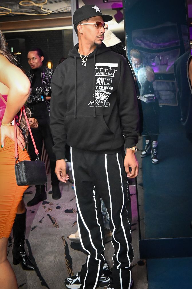 Person wearing black hoodie and striped track pants stands in dimly lit nightclub setting.