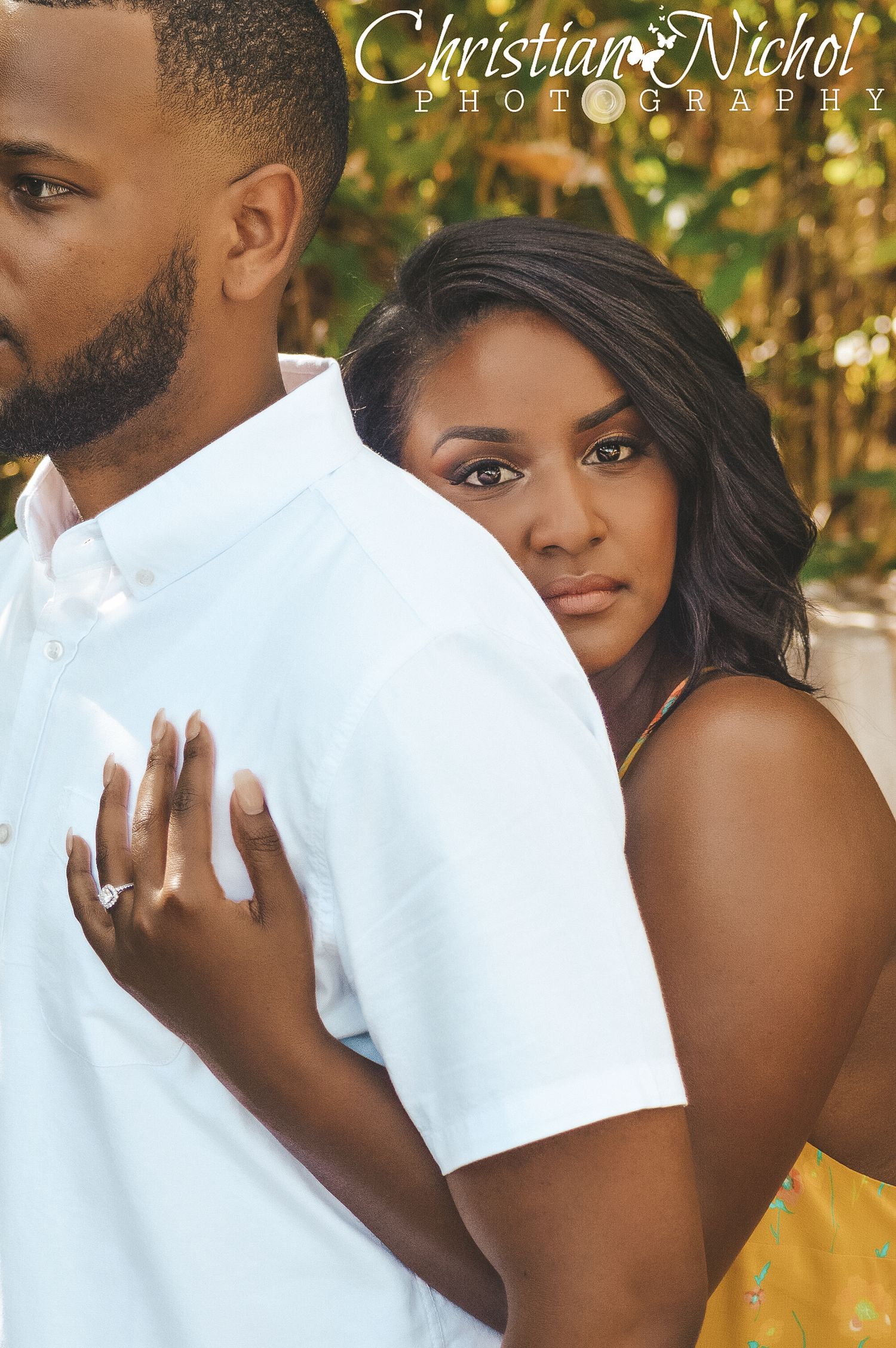 Engaged couple posing romantically, woman resting her head on mans shoulder showing diamond ring, professional engagement photo.