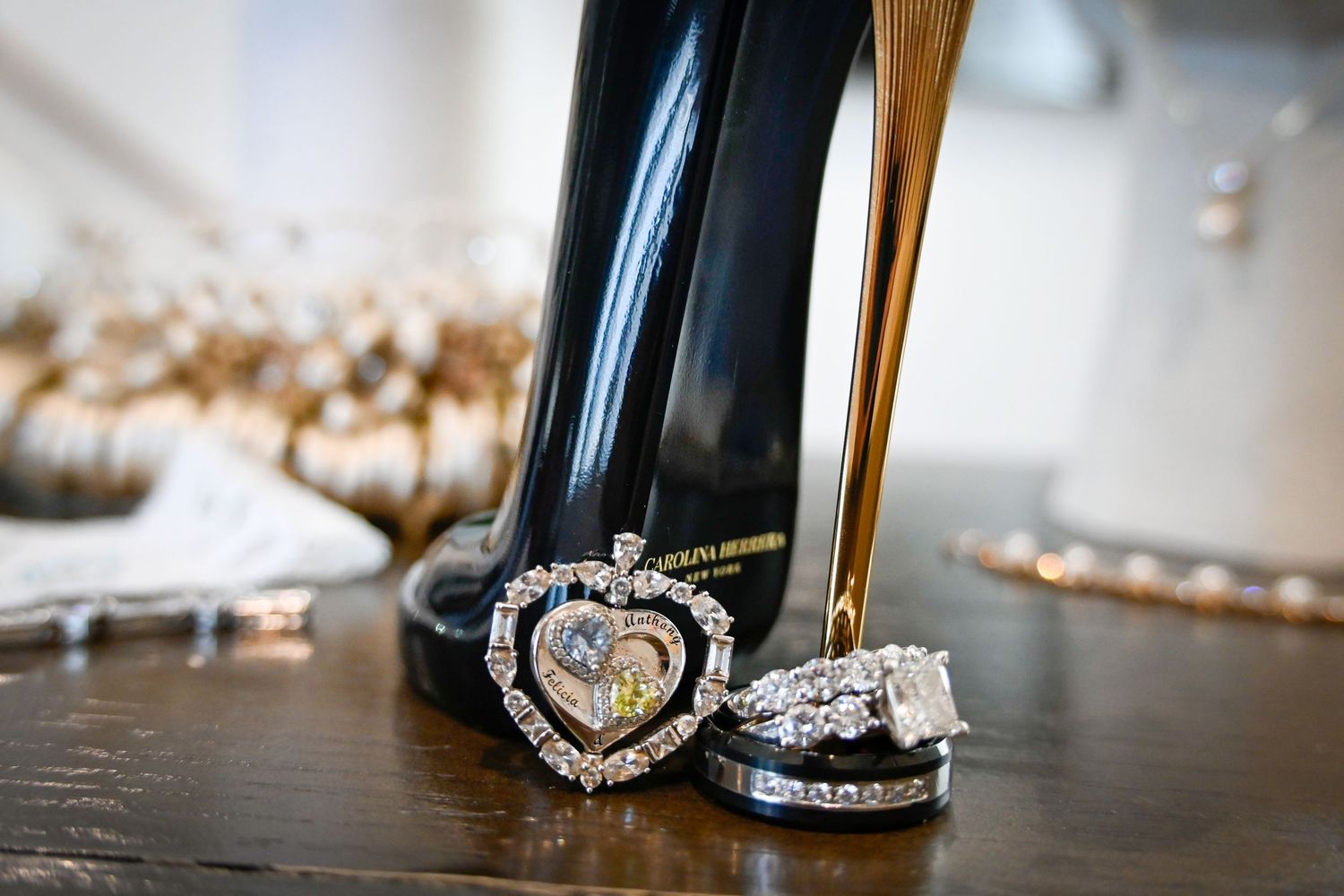 Black stiletto heels with heart-shaped diamond pendant and wedding ring set displayed on wooden surface.