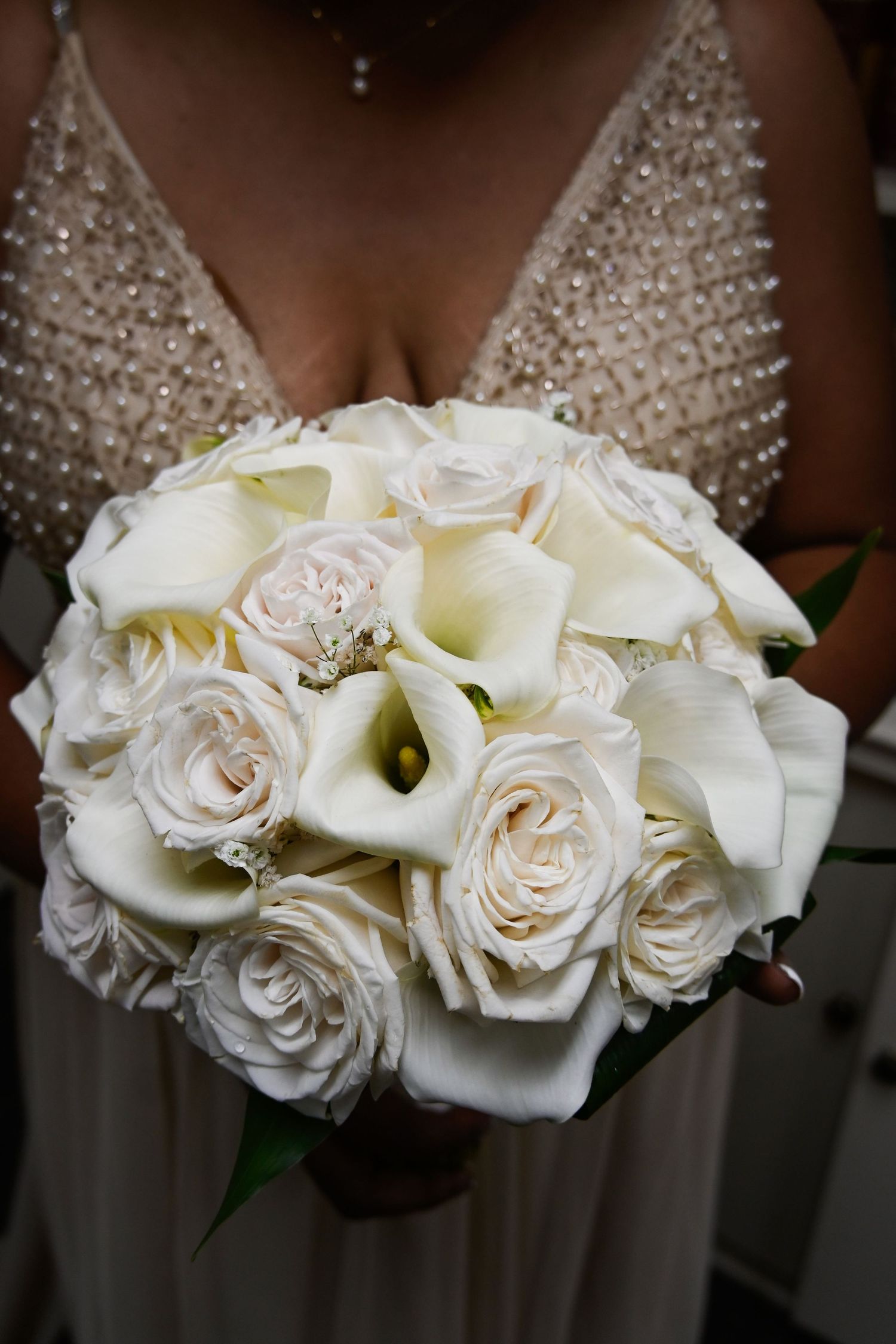 Bride holding a elegant round wedding bouquet of white roses and calla lilies against a beaded bridal gown.