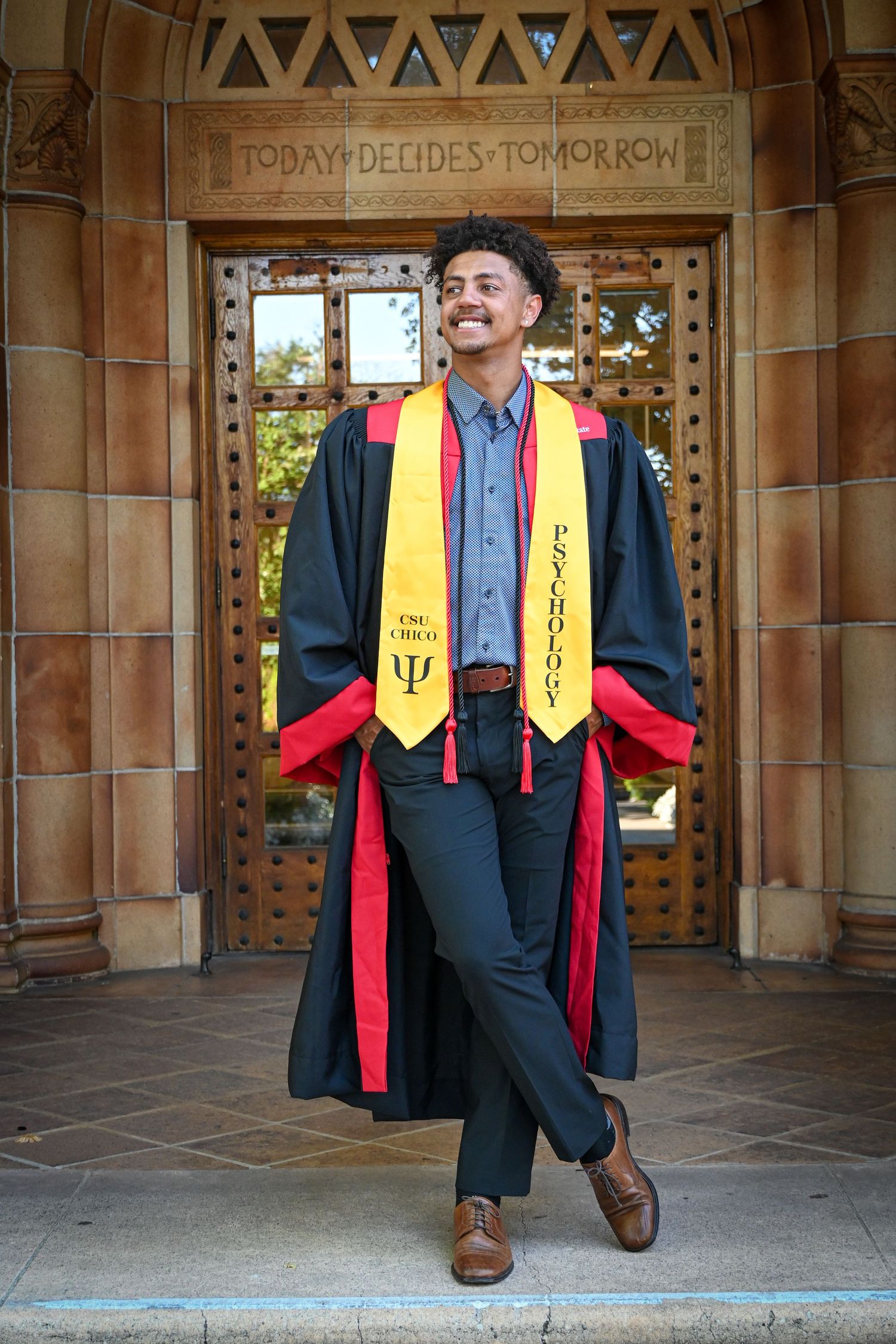 Graduate in academic regalia poses in three different positions under a stone archway on campus.