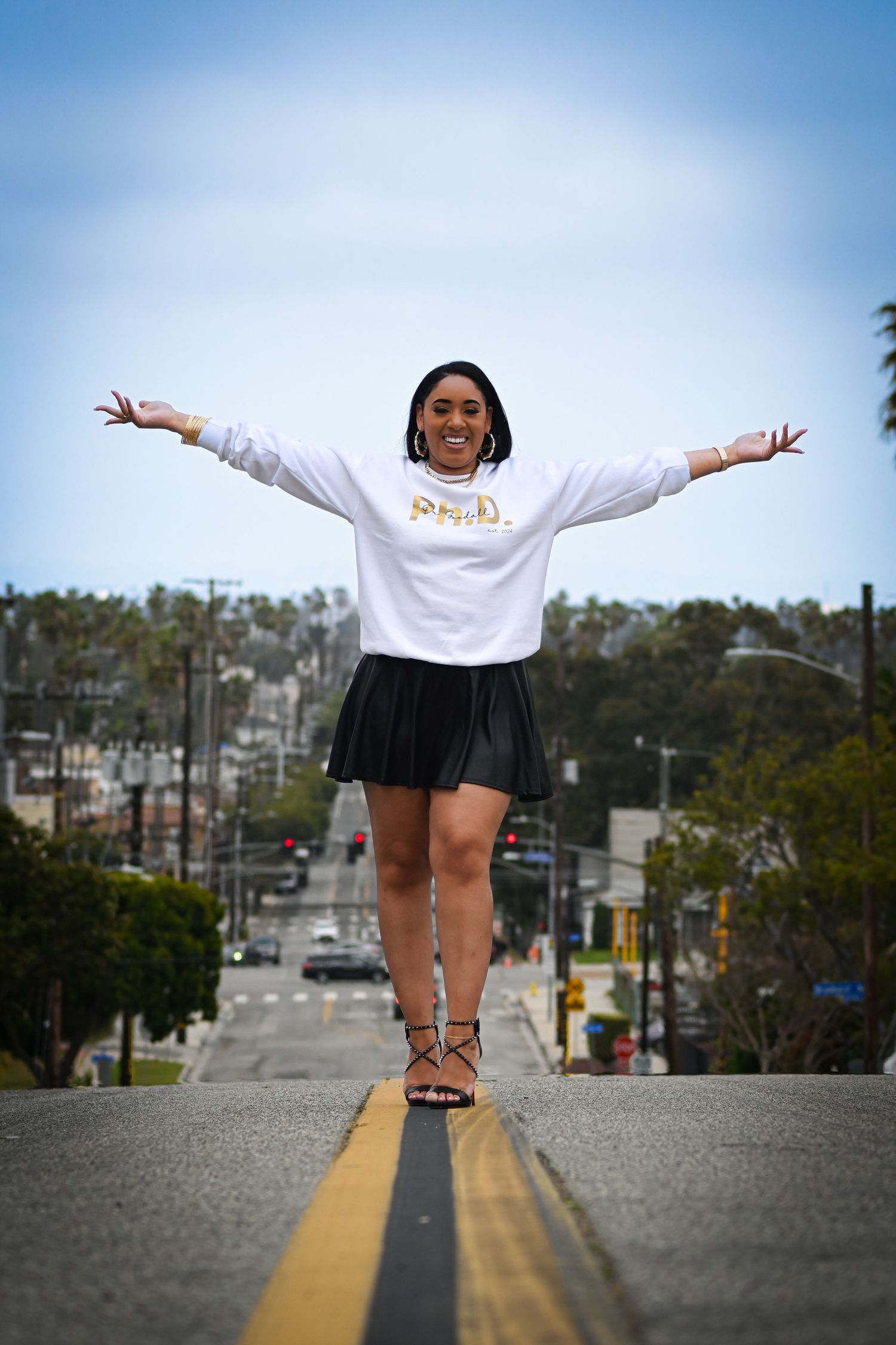 A joyful pose with arms spread wide on a street while wearing a Ph.D. sweatshirt.