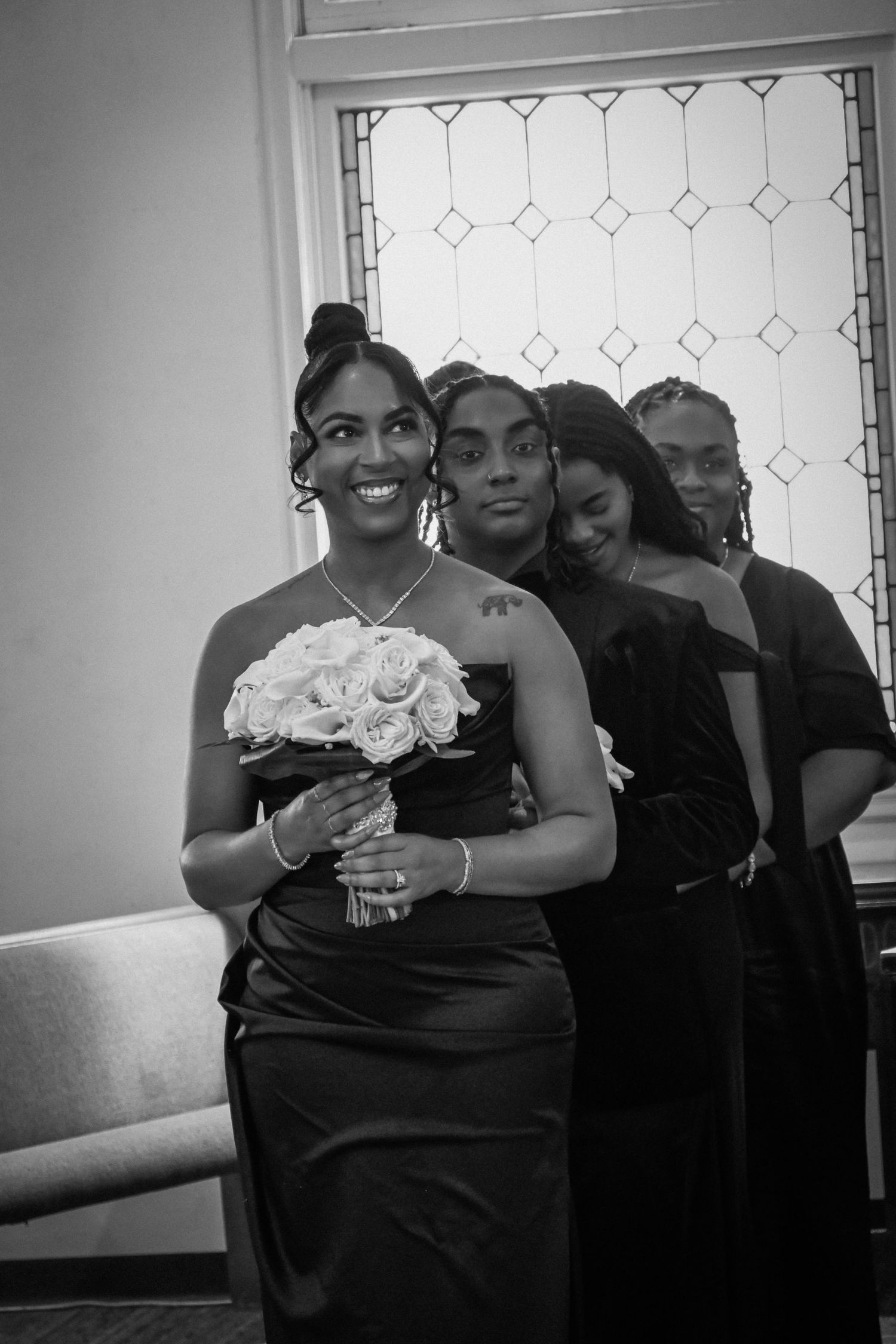 Black and white photo of bridesmaids in elegant black dresses, with lead bridesmaid holding white rose bouquet.