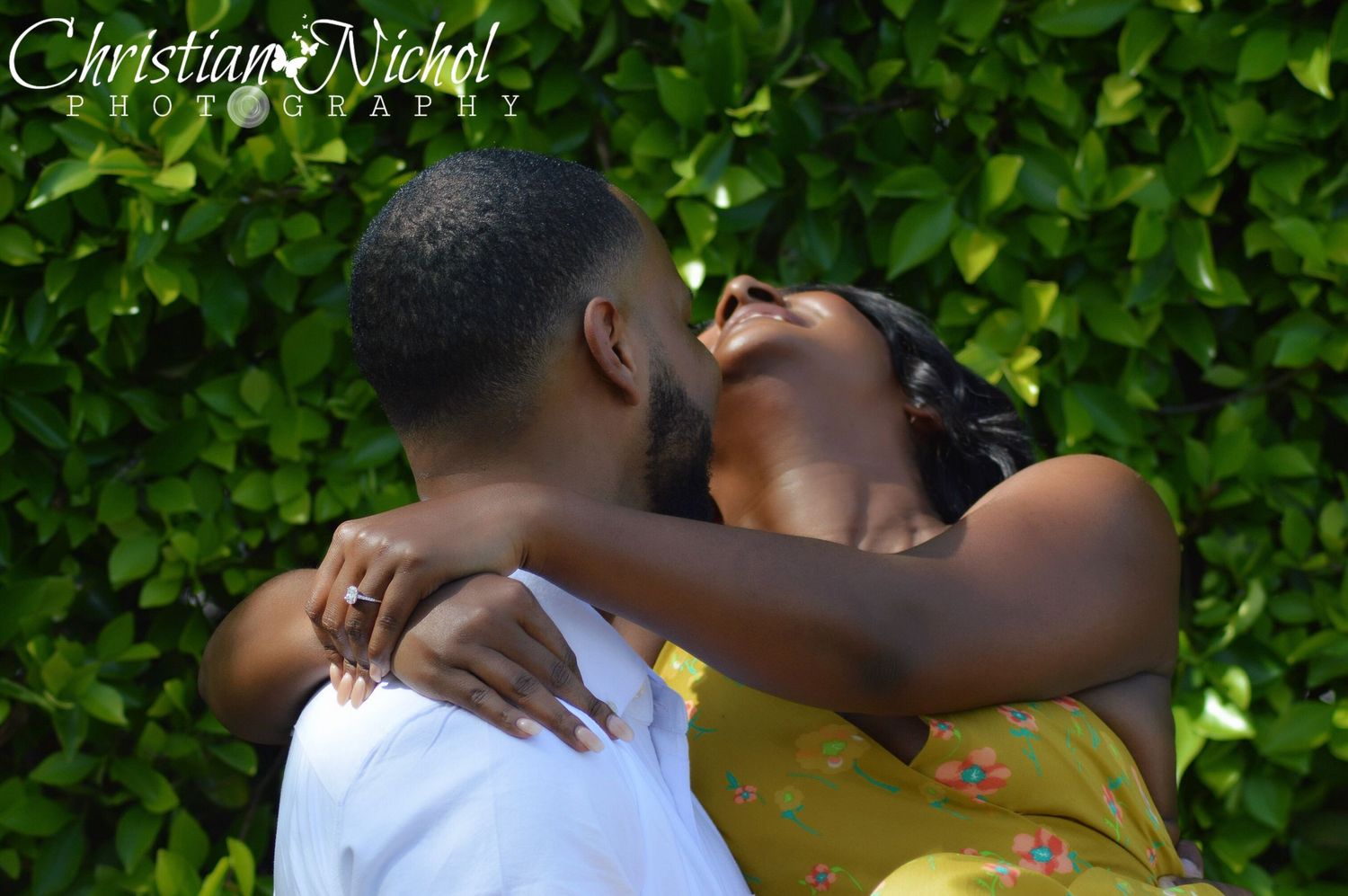 Couple sharing a romantic kiss outdoors with lush green ivy wall backdrop, captured by Christian Nichol Photography.