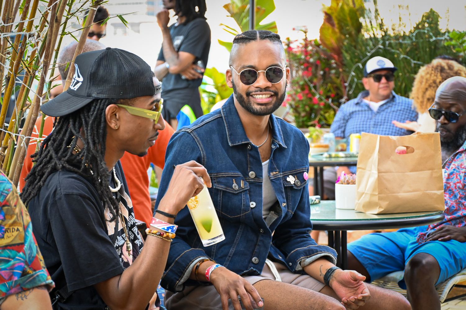 People enjoying drinks and conversation at an outdoor patio table on a sunny day.