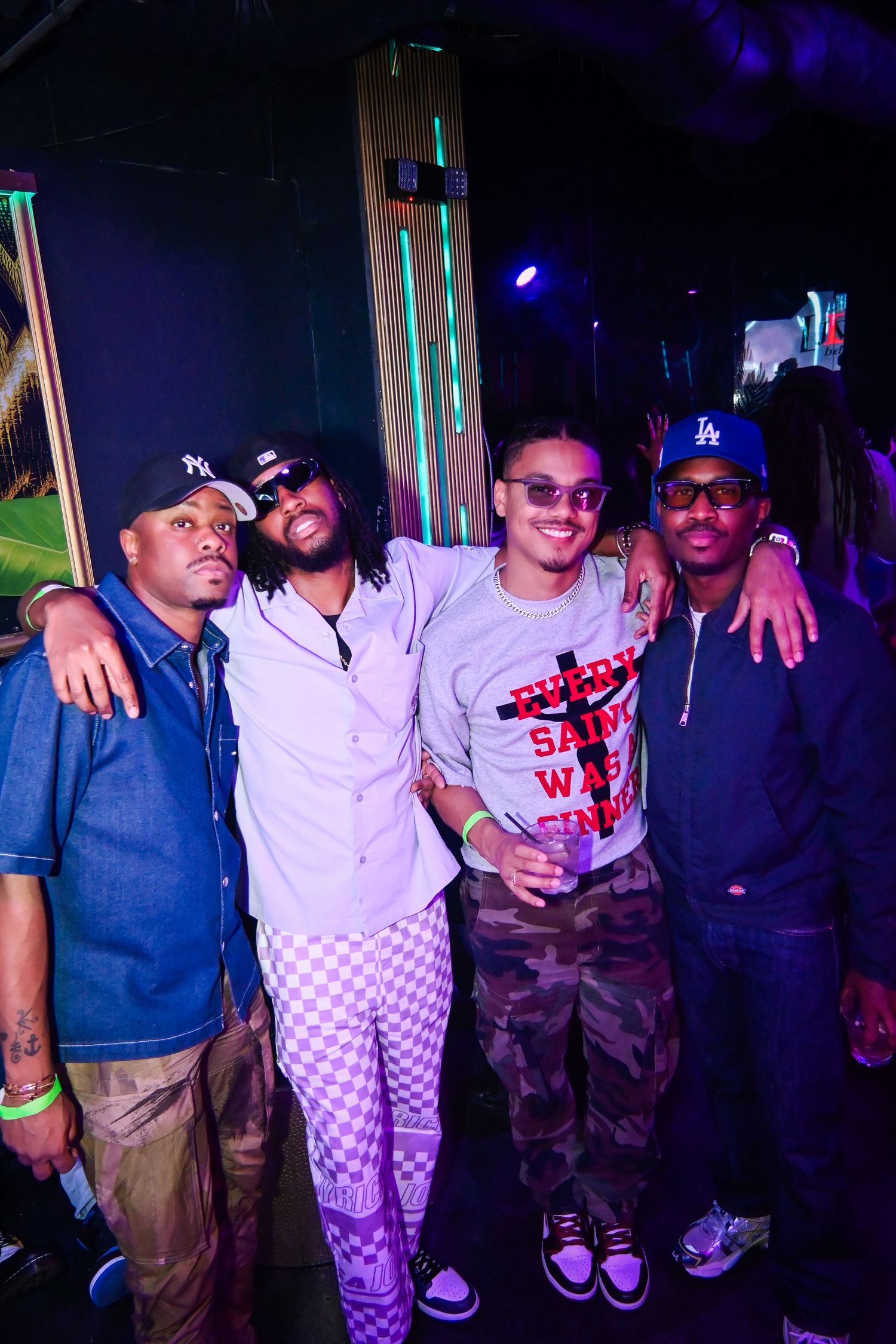 Group of friends posing together at a nightclub with dark lighting and neon accents in the background.