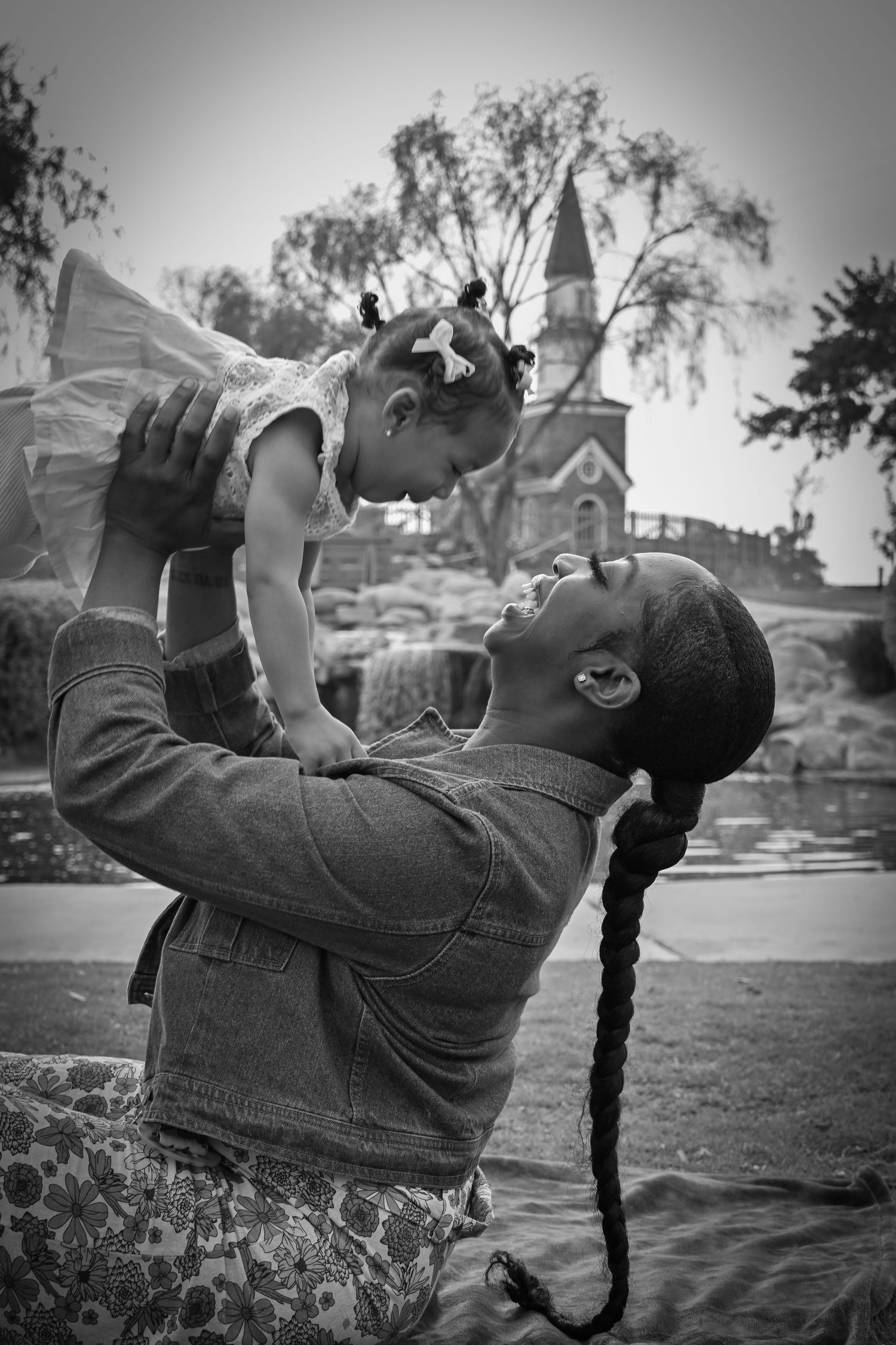 A tender black and white moment captured outdoors with a church steeple visible in the background.